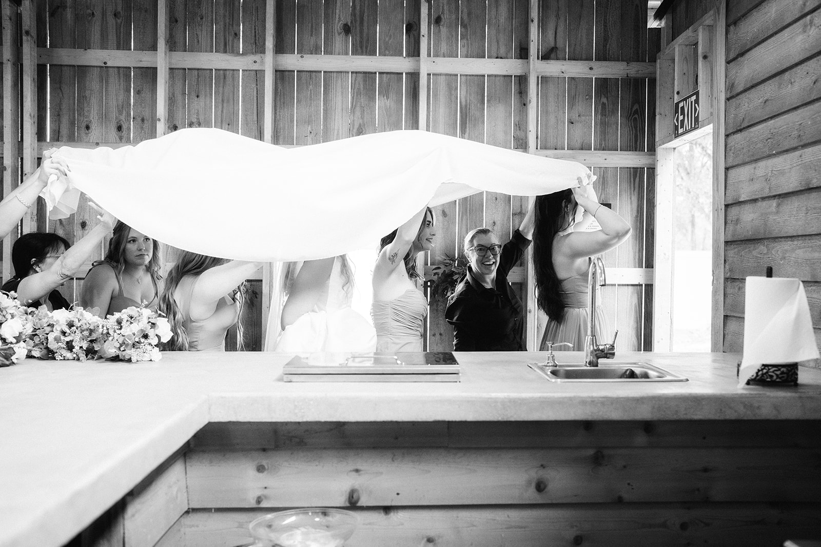 People gather around a table with a large cloth being held above them inside a wooden structure.