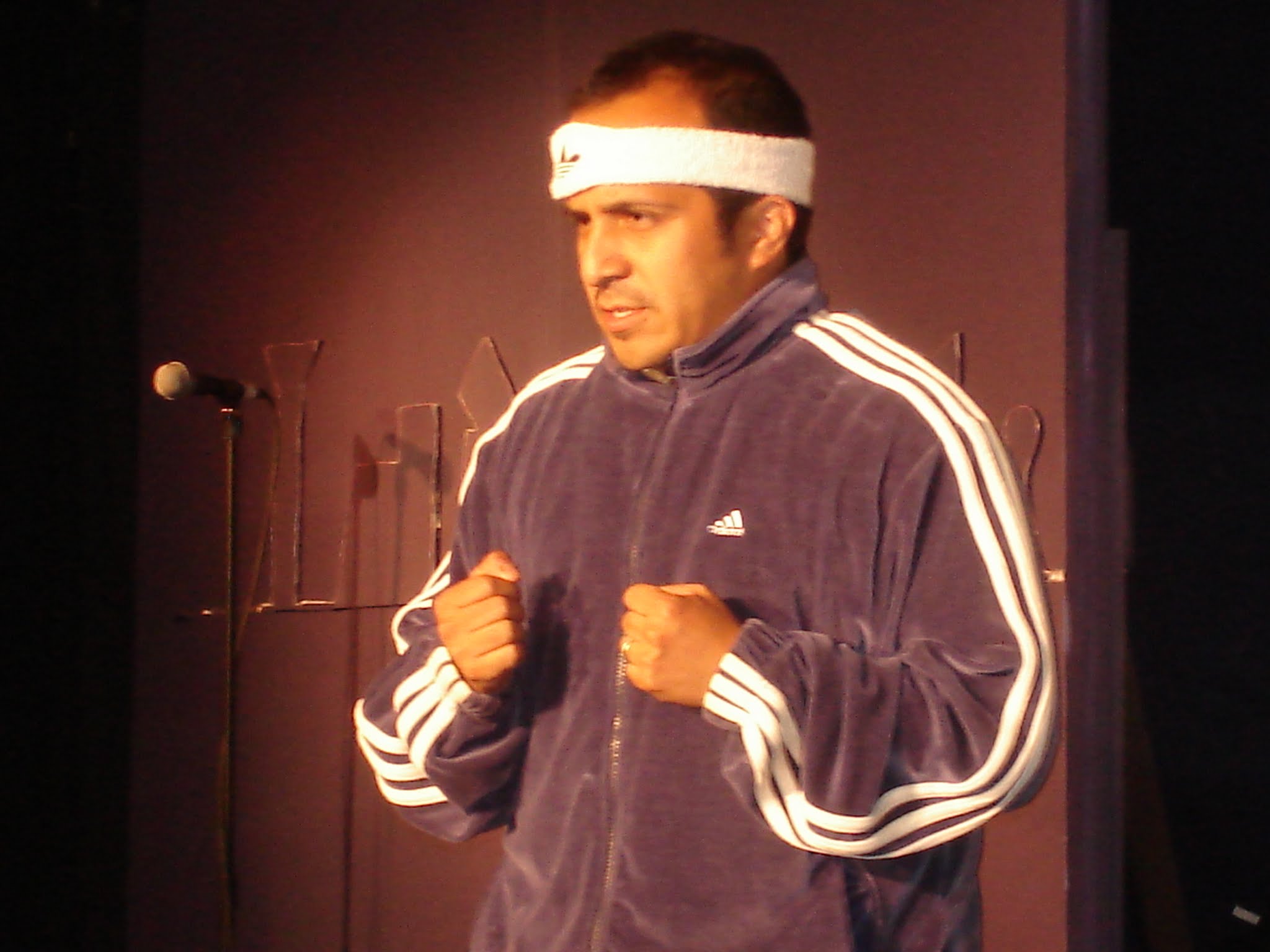 Person wearing a headband and a dark sports jacket with white stripes, fists clenched, standing indoors.