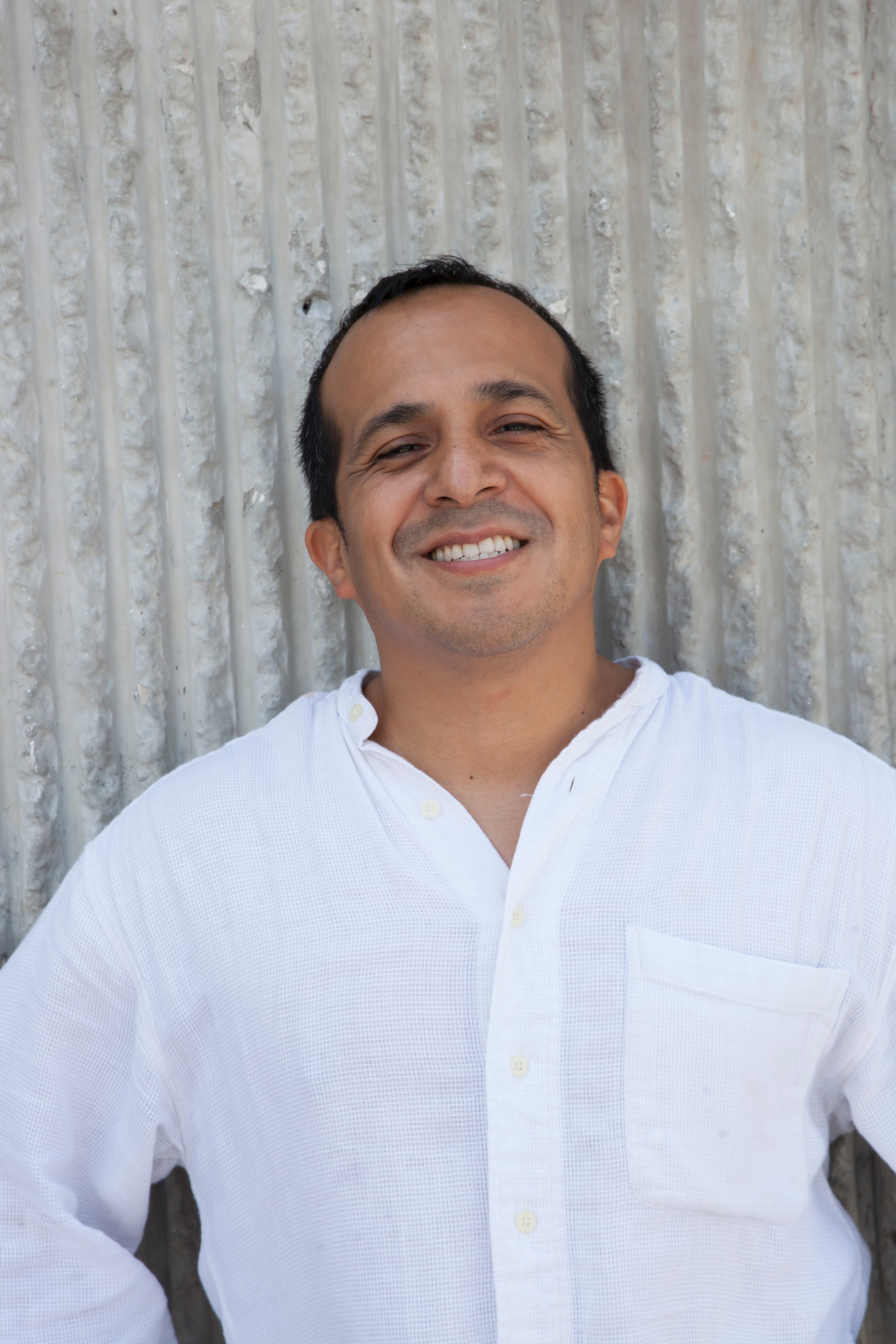 Smiling man in white shirt standing against textured wall background.