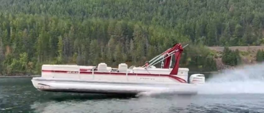 Motorboat moving fast on water with trees and forest in background.