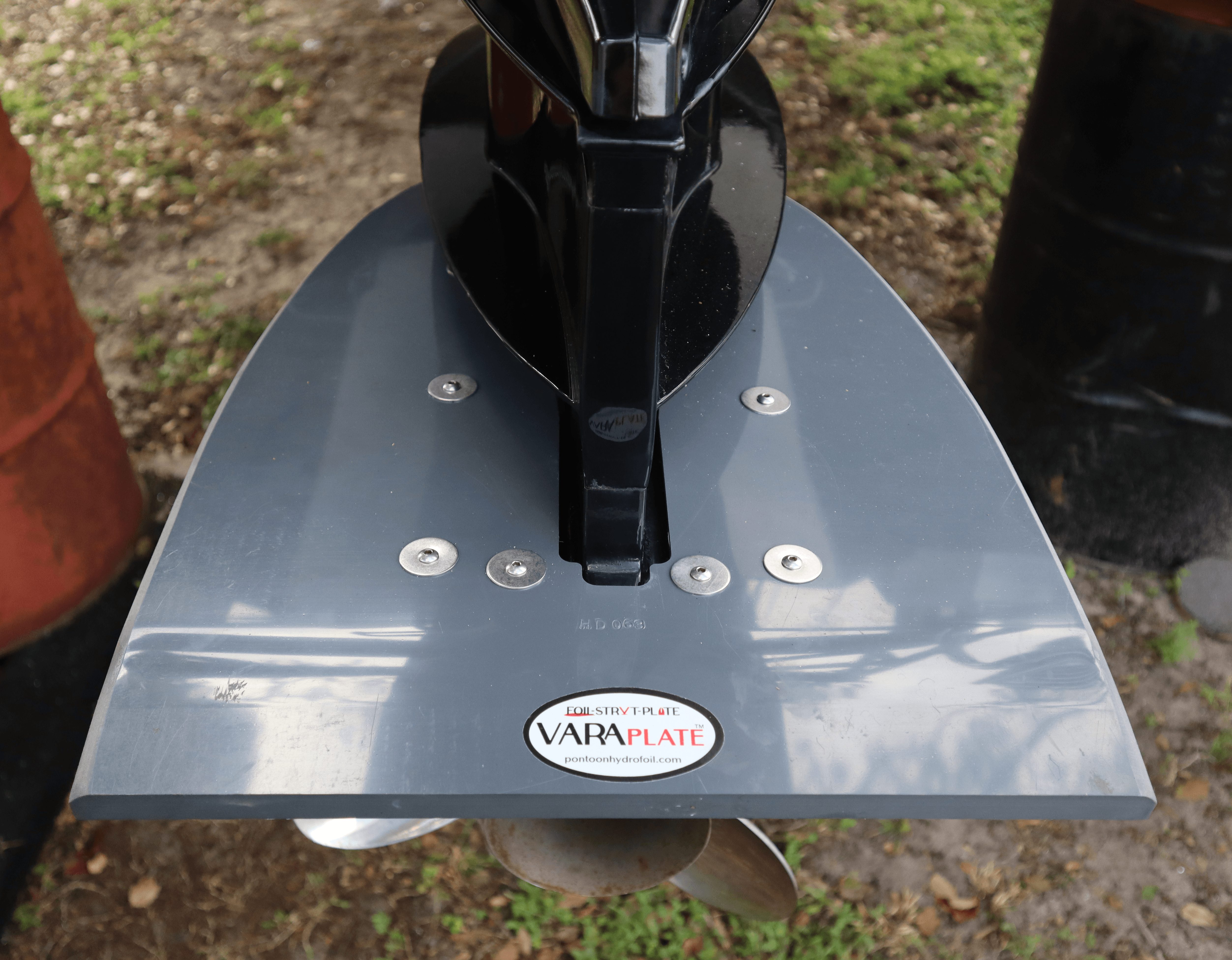 Metal paddle with a black handle, mounted on a reflective surface outdoors, with grass and objects in background.