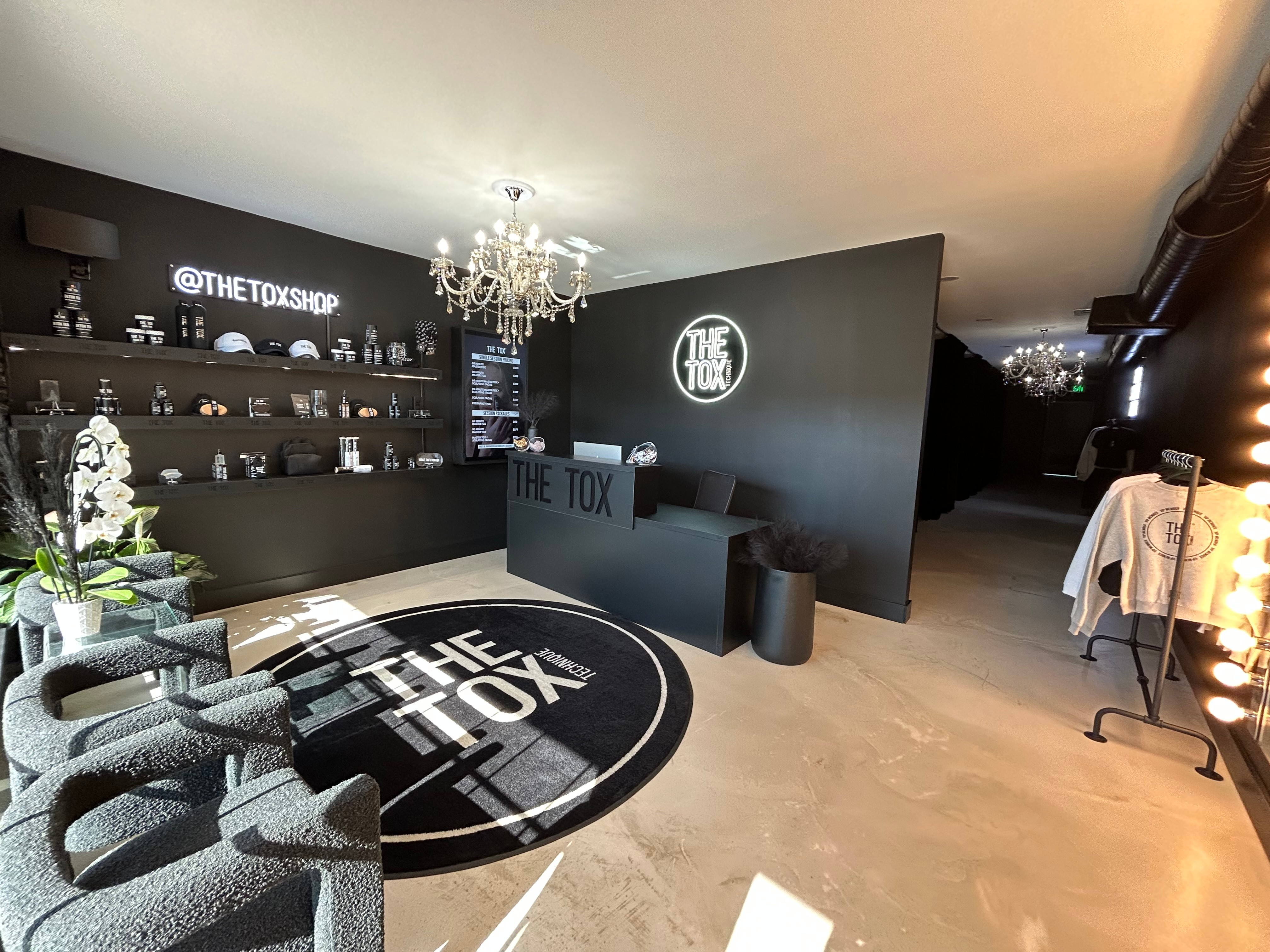 Interior of a shop with a chandelier, black walls, shelves with products, a round rug, and a black counter.