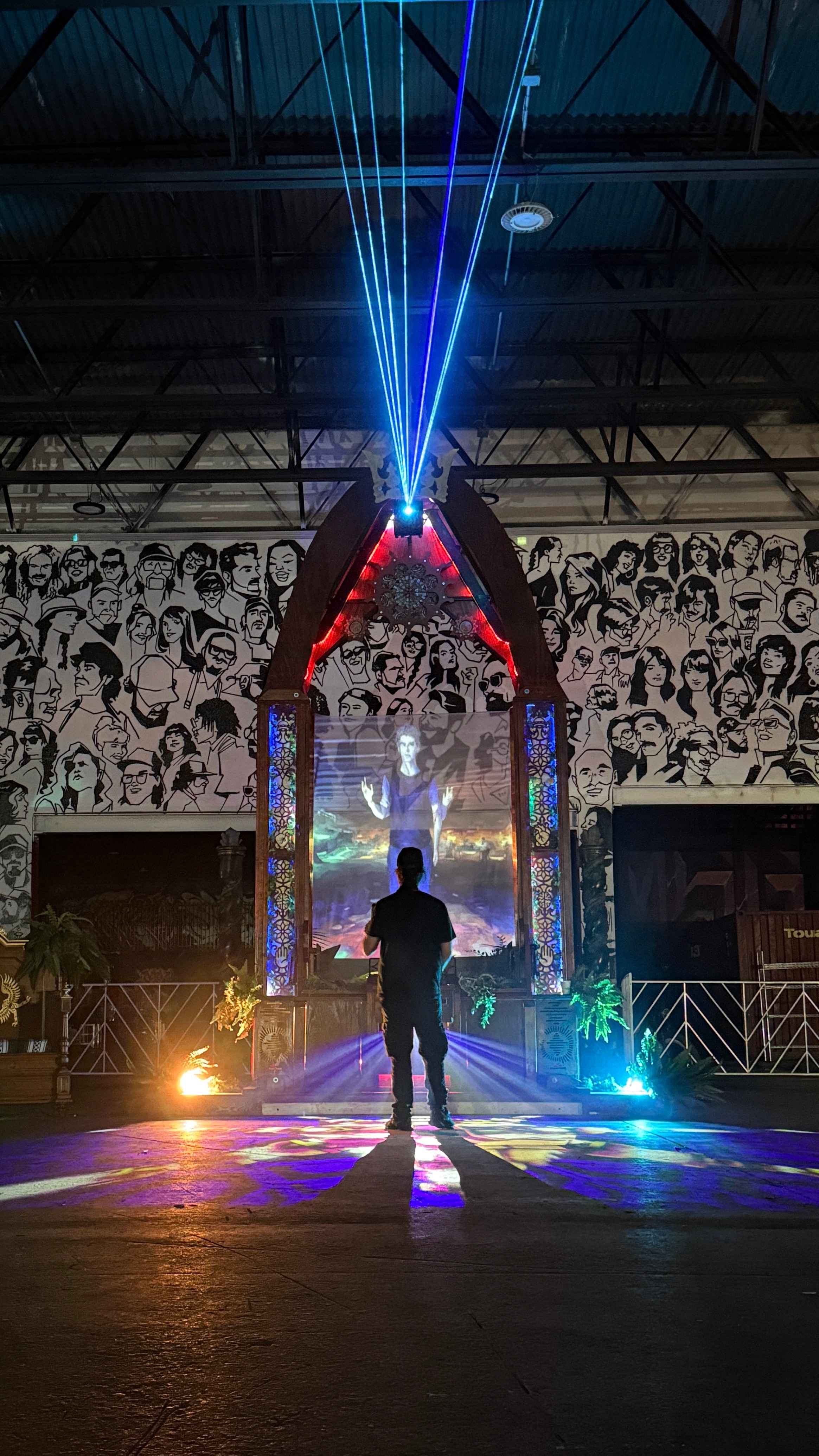 Person standing on stage with laser lights and a large black-and-white photo collage background.