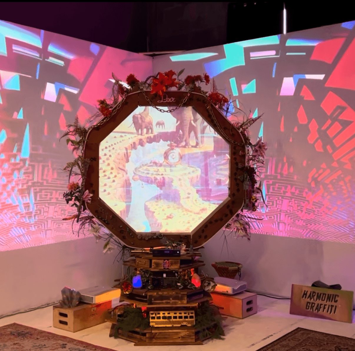 Hexagonal mirror surrounded by plants and decorations, with a colorful digital projection background.