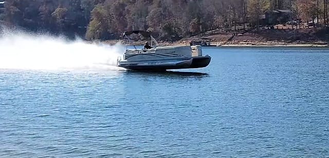 Motorboat speeding on water with spray behind, trees in background.