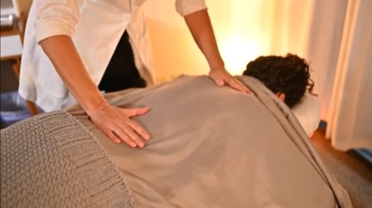 Person receiving a massage on their back with hands applying pressure, in a warm room.