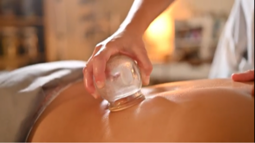 Person holding a glass cup on a person's back during a massage or therapy session.