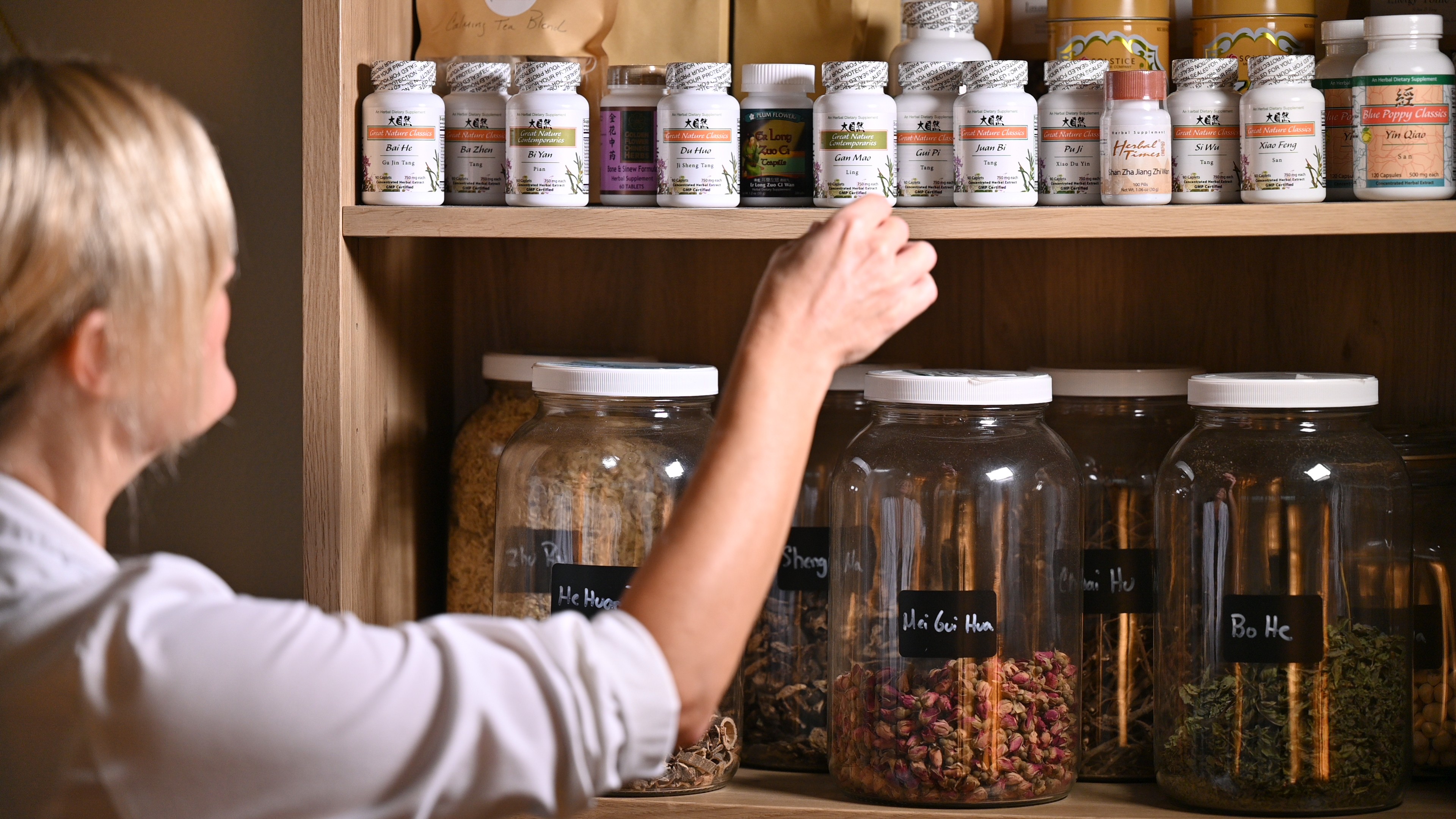 Child reaching for jars and bottles on a wooden shelf, containing various pills and supplements.