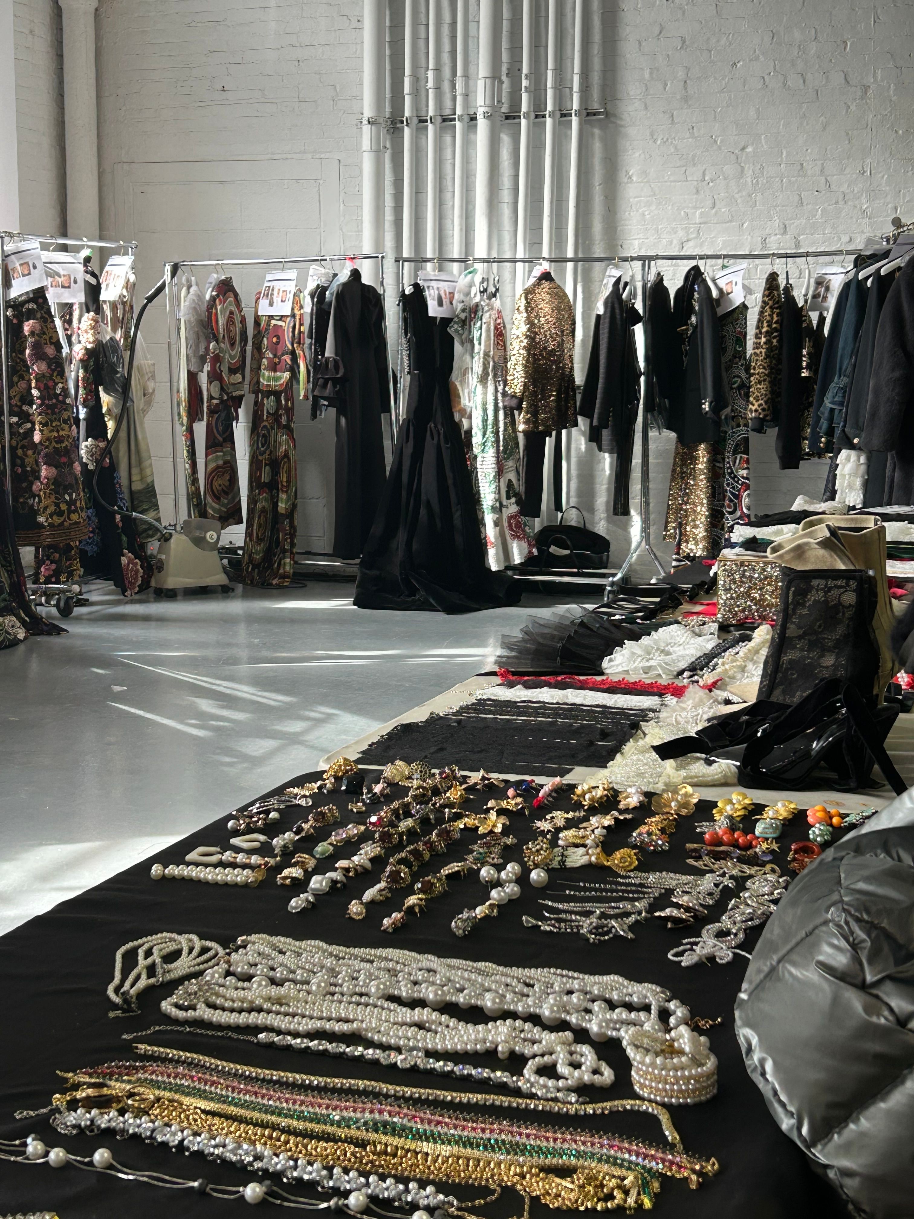 Jewelry and clothing displayed on tables and racks in a store, with various necklaces, bracelets, and garments visible.
