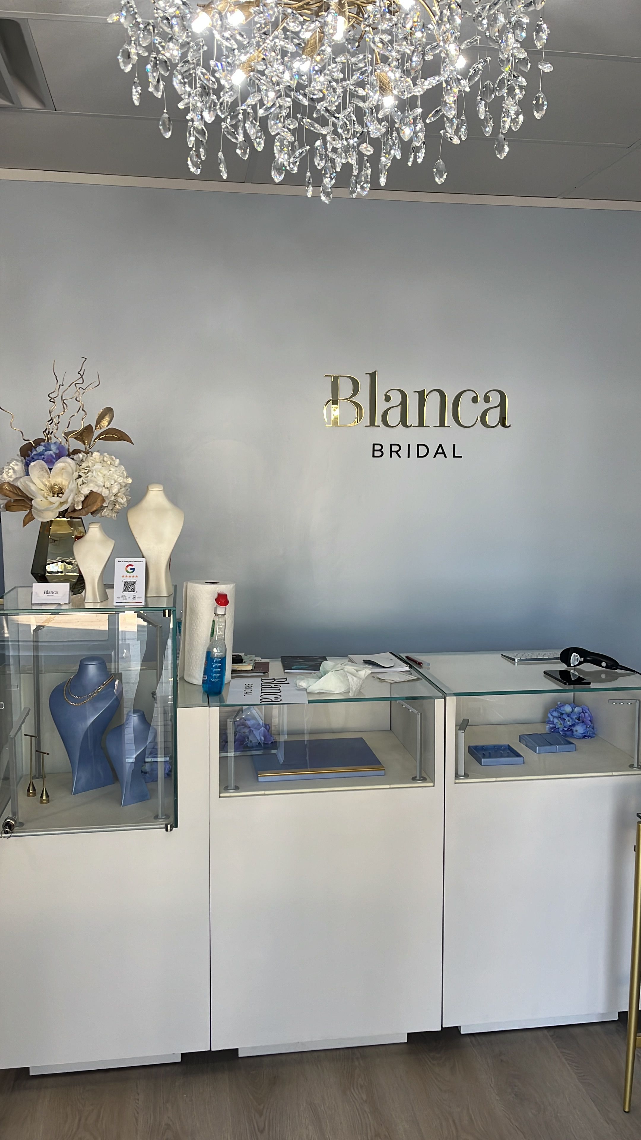 Beauty salon interior with a white wall, shelves, and a decorative flower arrangement, with the name 'Blanca Borda' on the wall.