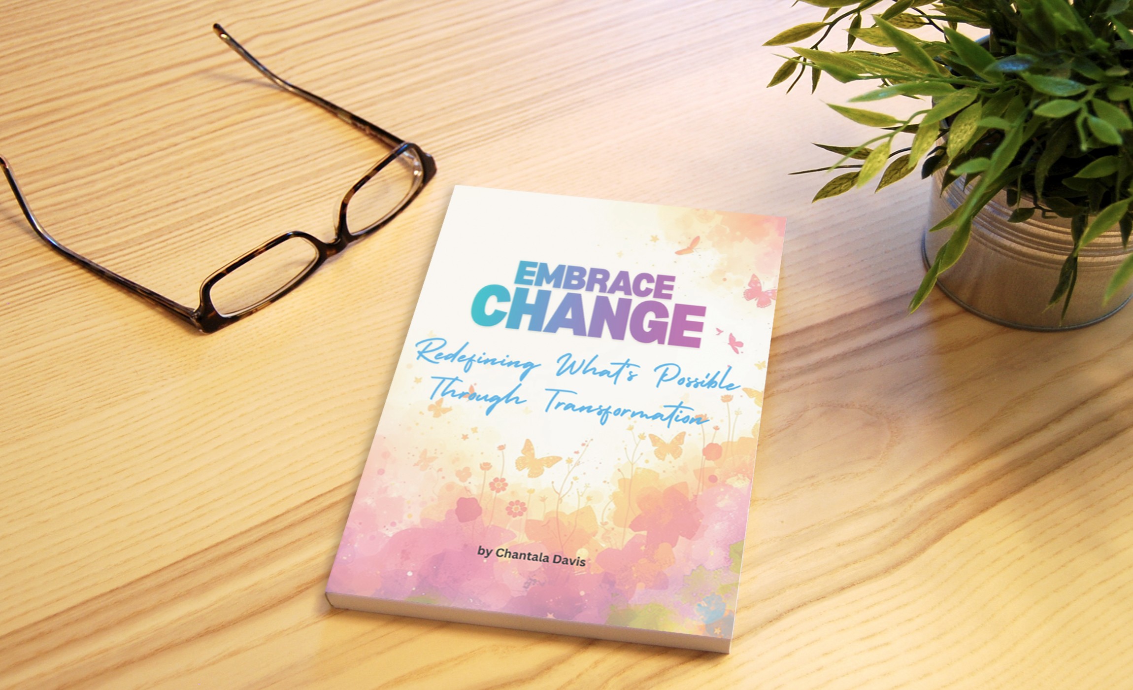 Book titled 'Embrace Change' on a wooden desk with glasses and a potted plant nearby.
