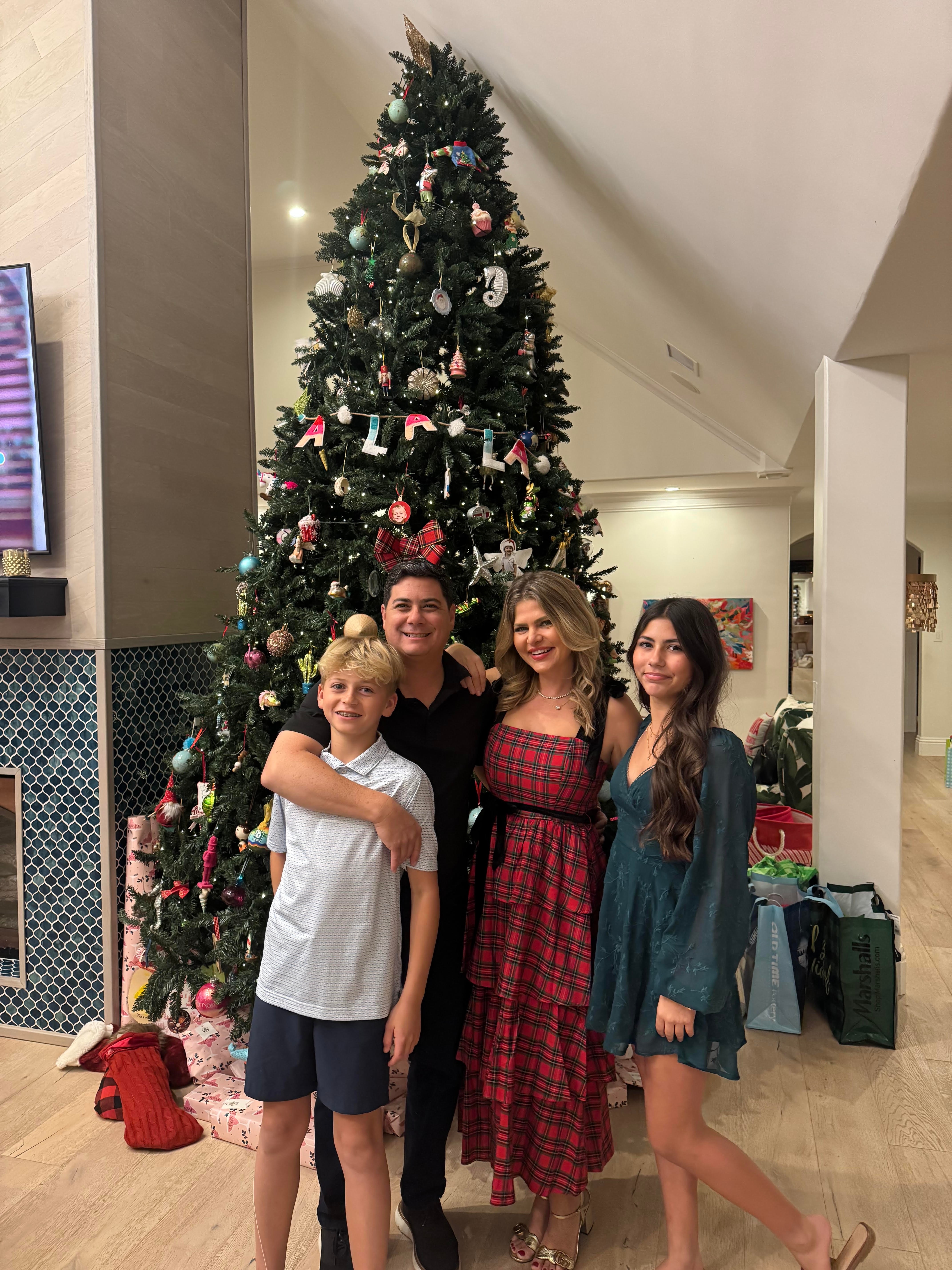Four people stand in front of a decorated Christmas tree indoors, smiling and posing for the photo.