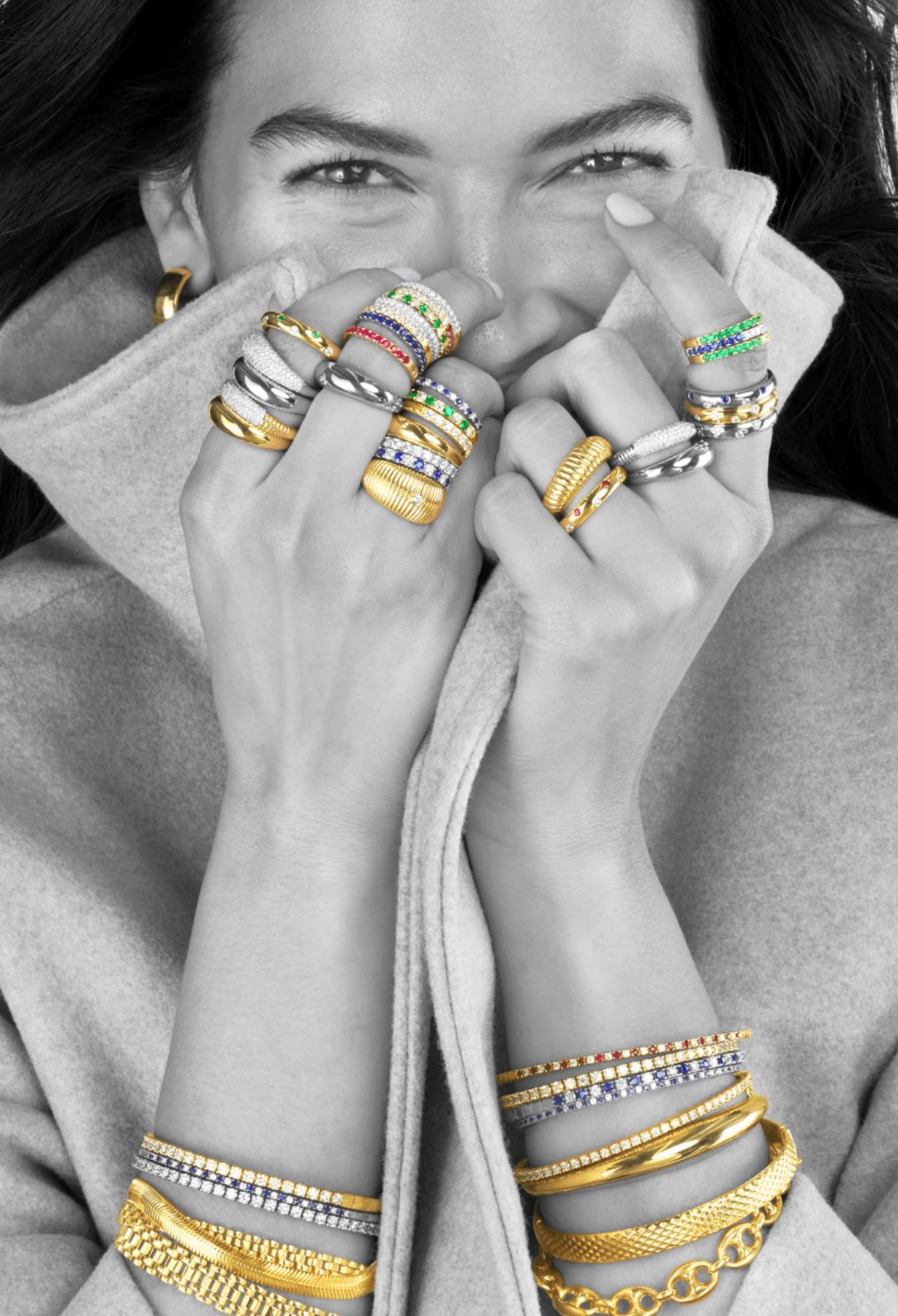 Person smiling, covering face with hands, wearing multiple rings and bracelets, in black and white.