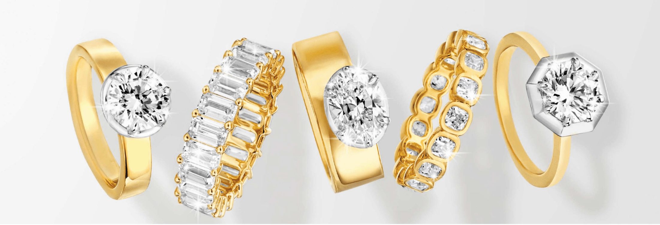 Five gold rings with diamonds and gemstones, displayed in a row, with different designs and settings.