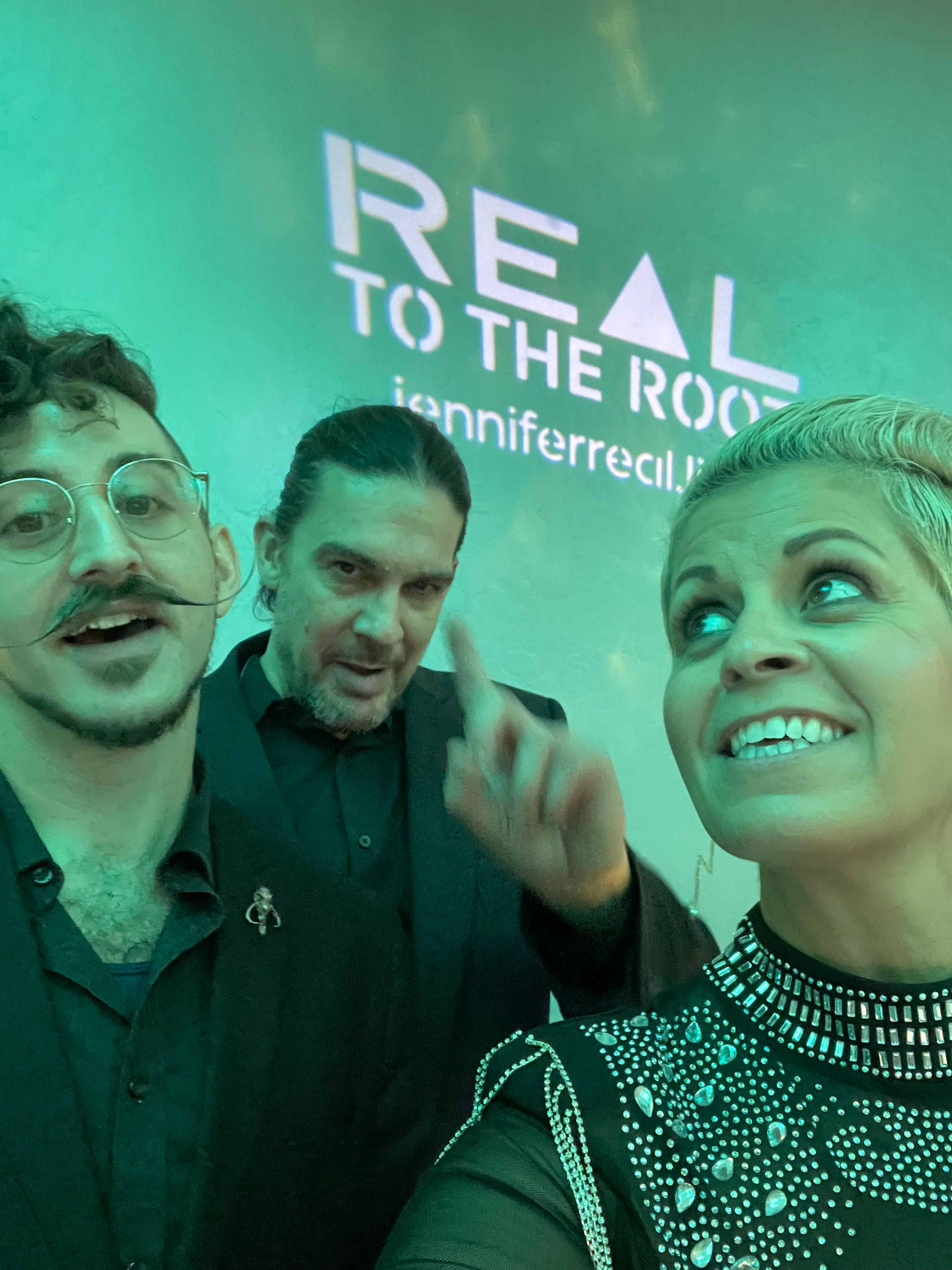 Two women and a man smiling, with a green background and text reading 'RE' and 'TO THE ROCK'.