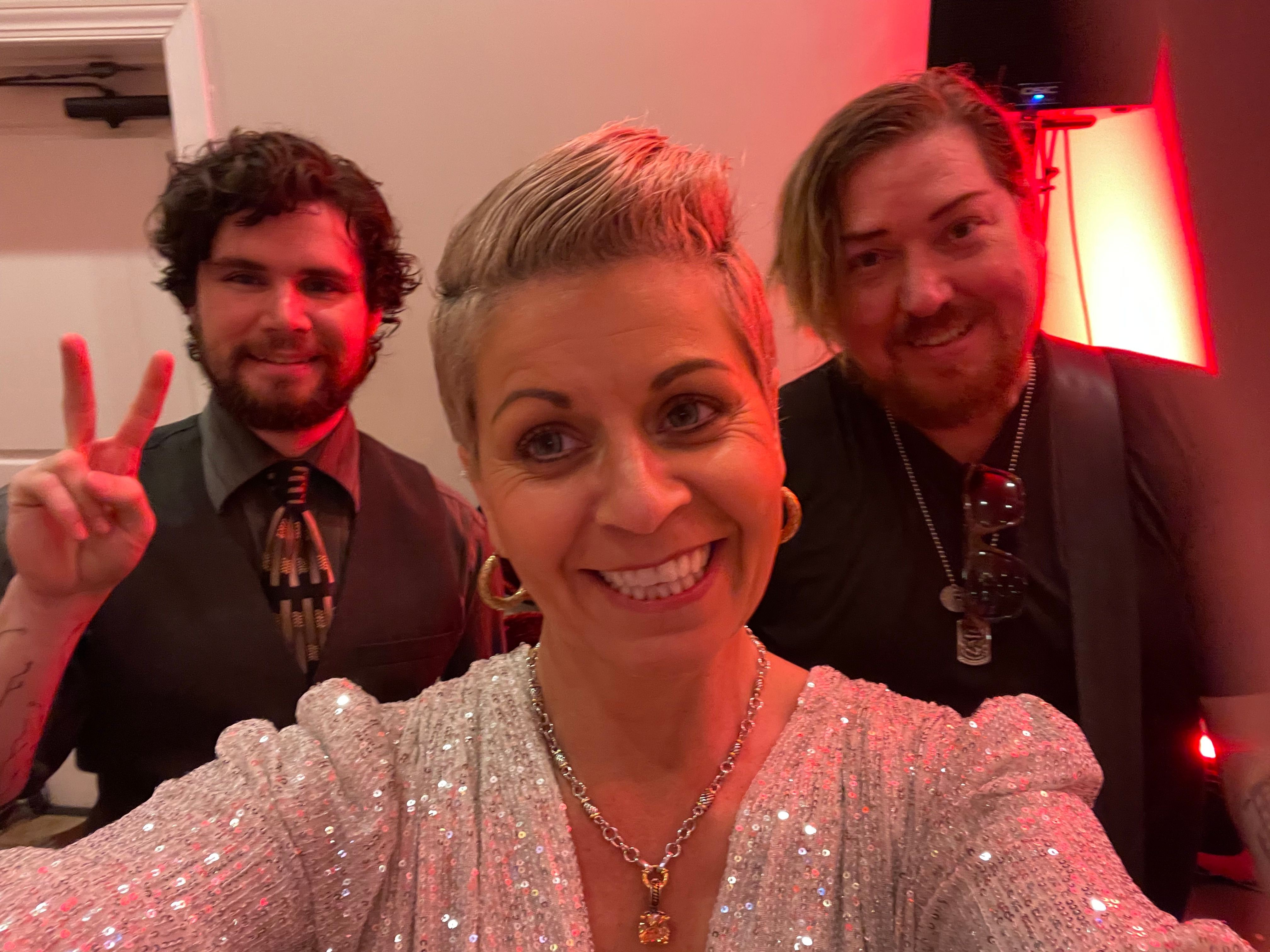 Three people smiling, one making a peace sign, in a dimly lit room with red lighting, upside down.