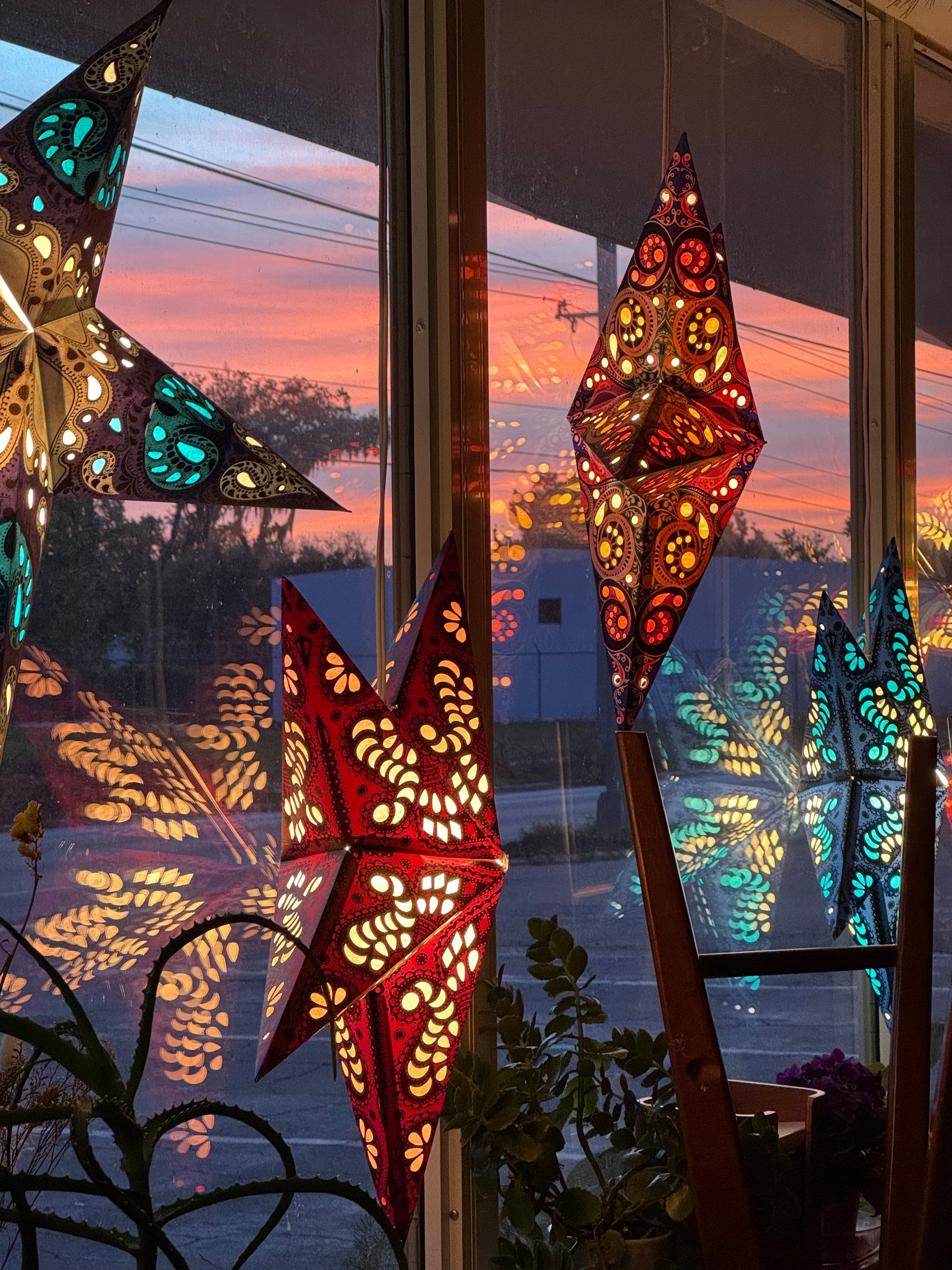 Colorful decorative lanterns hanging in front of a window with a sunset view, reflections visible on the glass.
