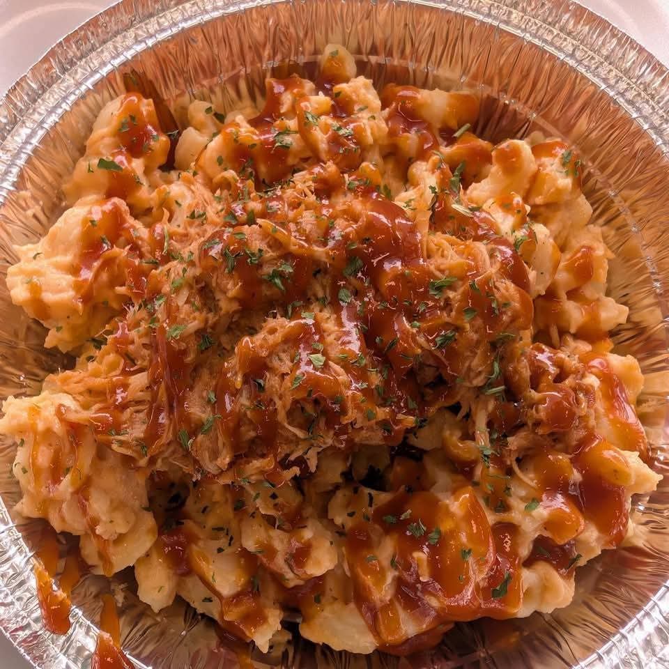 Close-up of a pasta dish with sauce and herbs in a foil container.