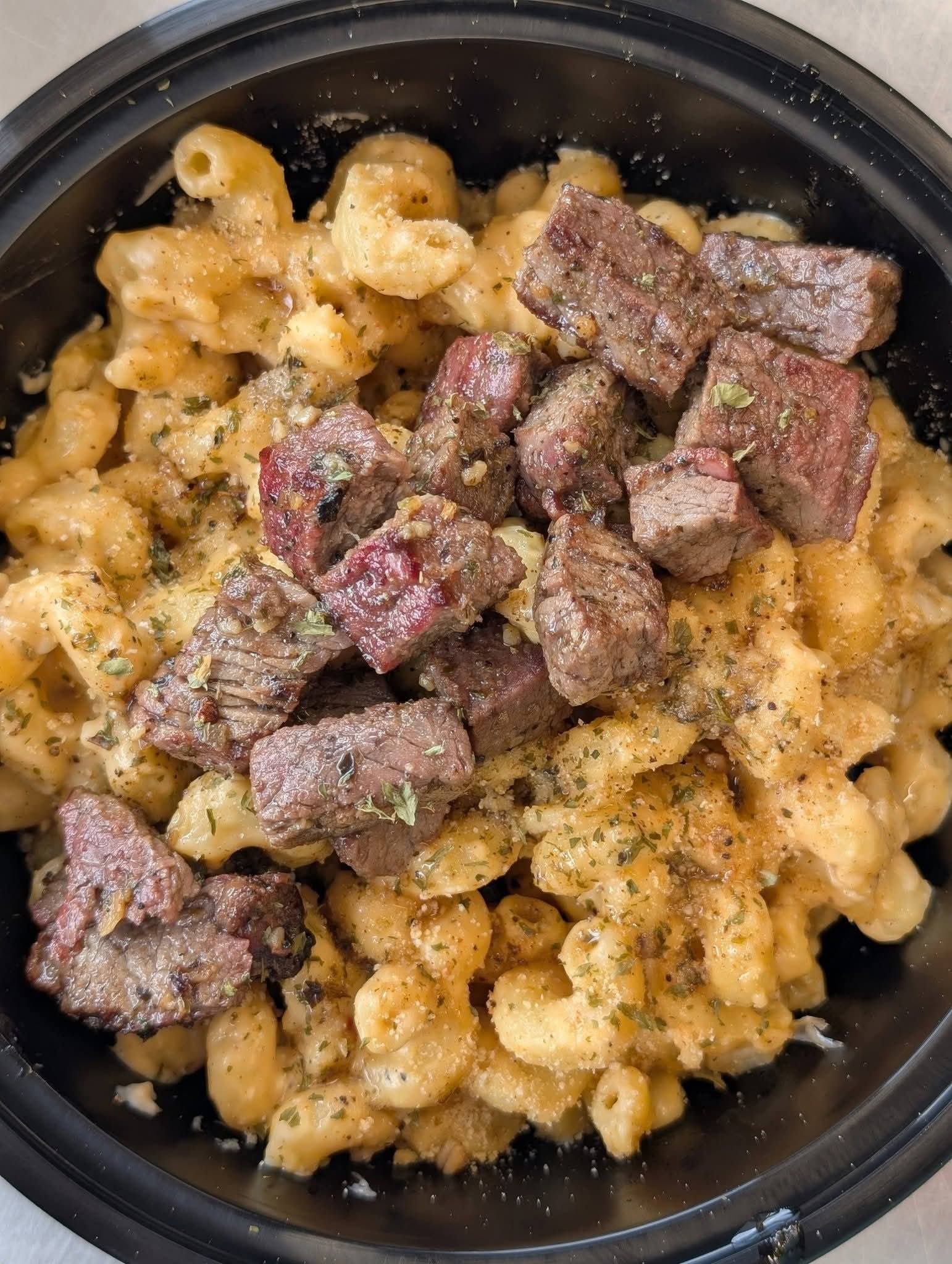 Cooked macaroni and cheese topped with cooked beef chunks in a black bowl.