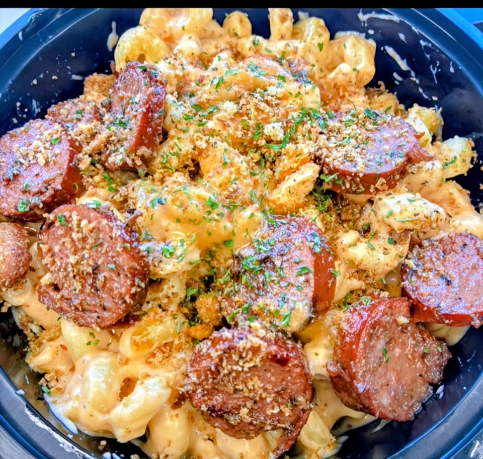 Creamy pasta with sausage slices, topped with herbs and grated cheese in a black bowl.