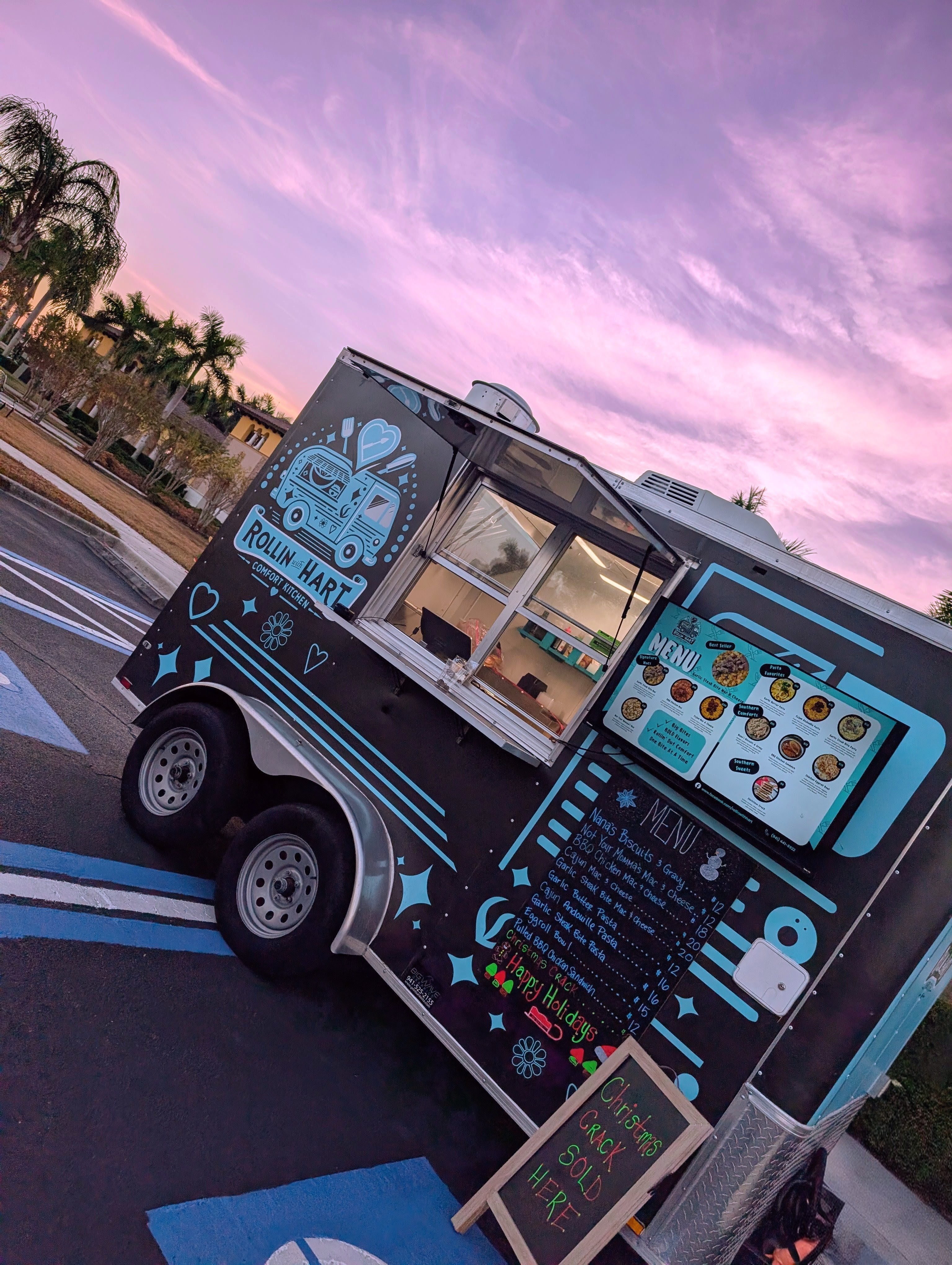 Food truck with a blue and black design, serving food on a street with a pink and purple sky.