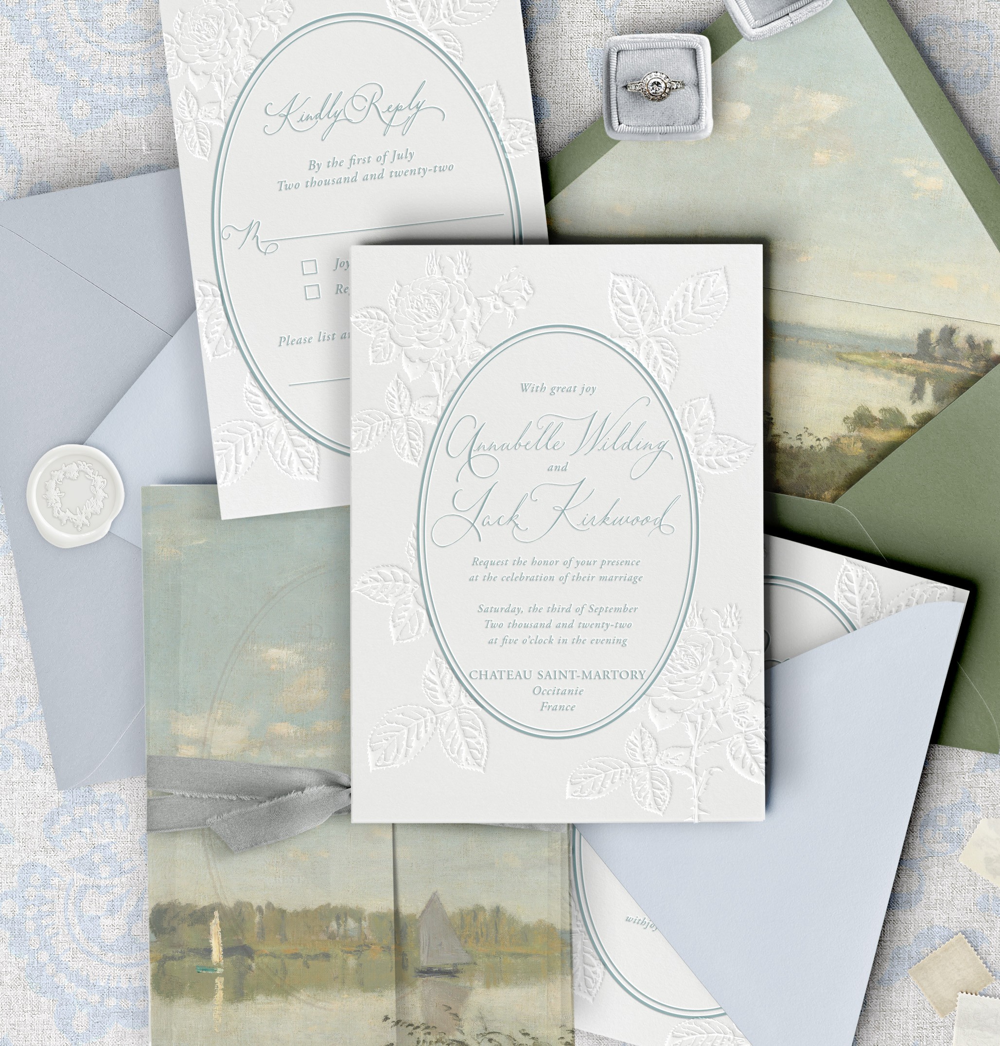 Wedding invitation with embossed floral design, surrounded by envelopes and a scenic landscape photograph, all in pastel colors.
