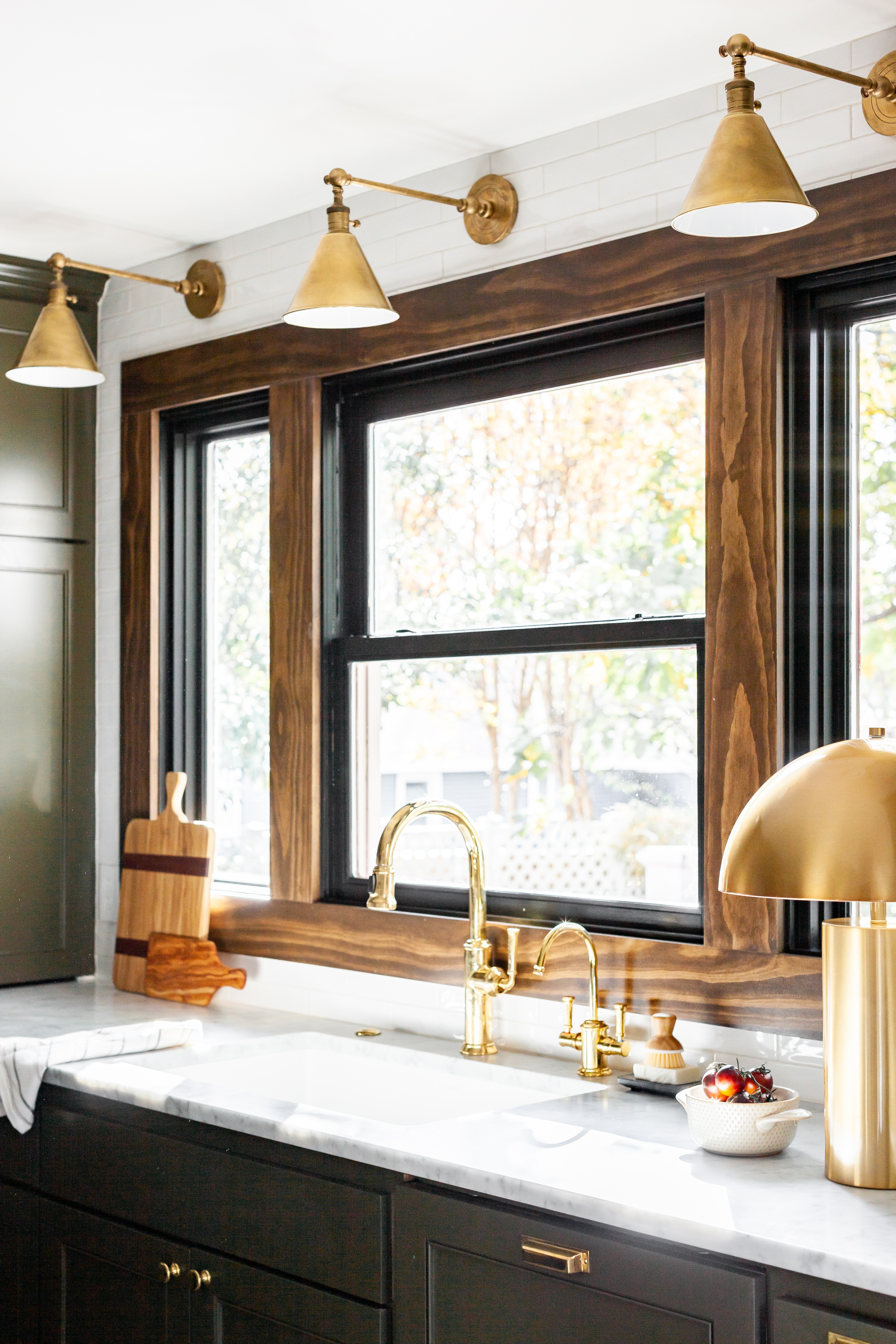 Kitchen window with wooden frame, gold fixtures, and a marble countertop, illuminated by a gold wall lamp and ceiling lights.