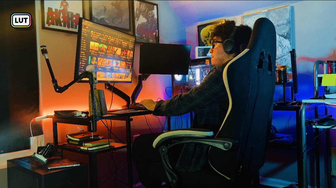 Person wearing a VR headset sitting at a desk with multiple monitors and colorful lighting, gaming setup.