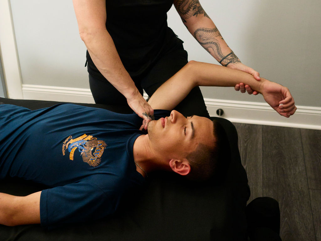 Person lying on a table receiving a neck massage from a therapist, with a tattooed arm visible.