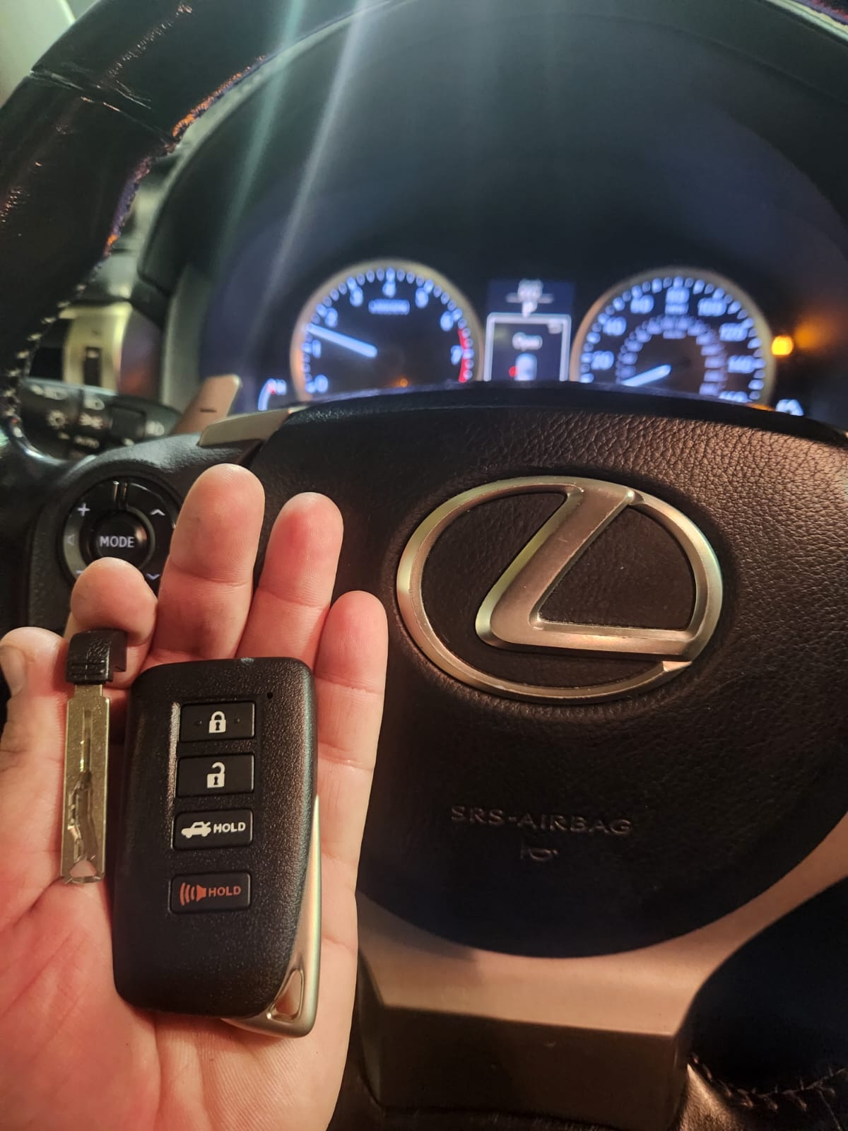 Person holding car key fob in front of steering wheel with dashboard visible in background.