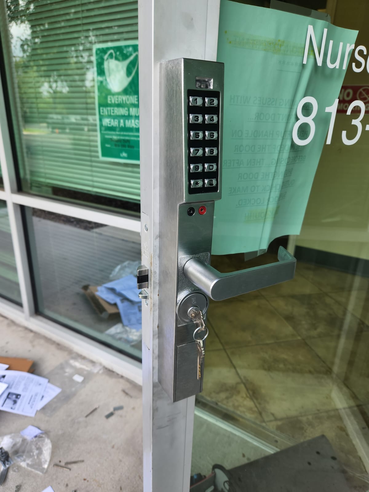 Door with keypad lock and glass window, showing a sign and interior reflection.