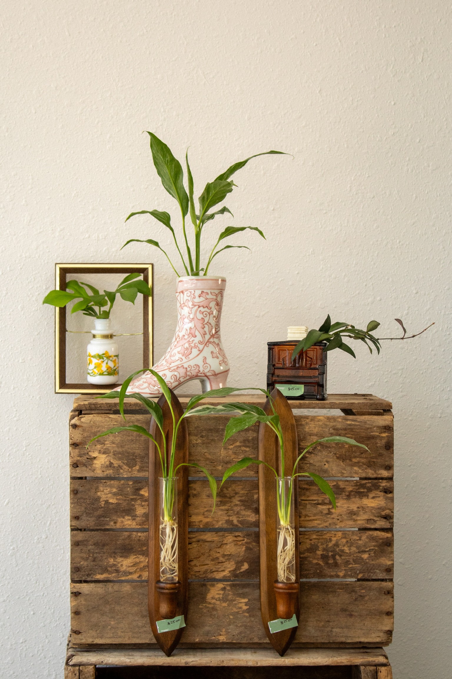 Decorative arrangement with a plant in a pink vase, a small plant, and a mirror on a wooden surface.