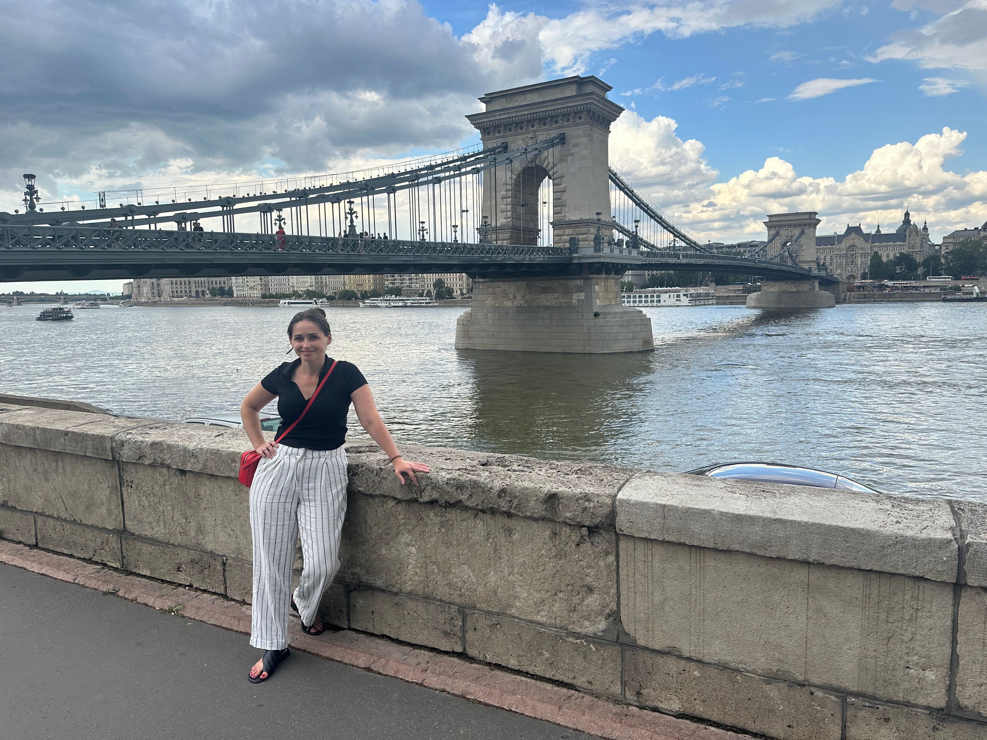 Person standing on a paved walkway near water with a bridge and cityscape in the background, upside down.