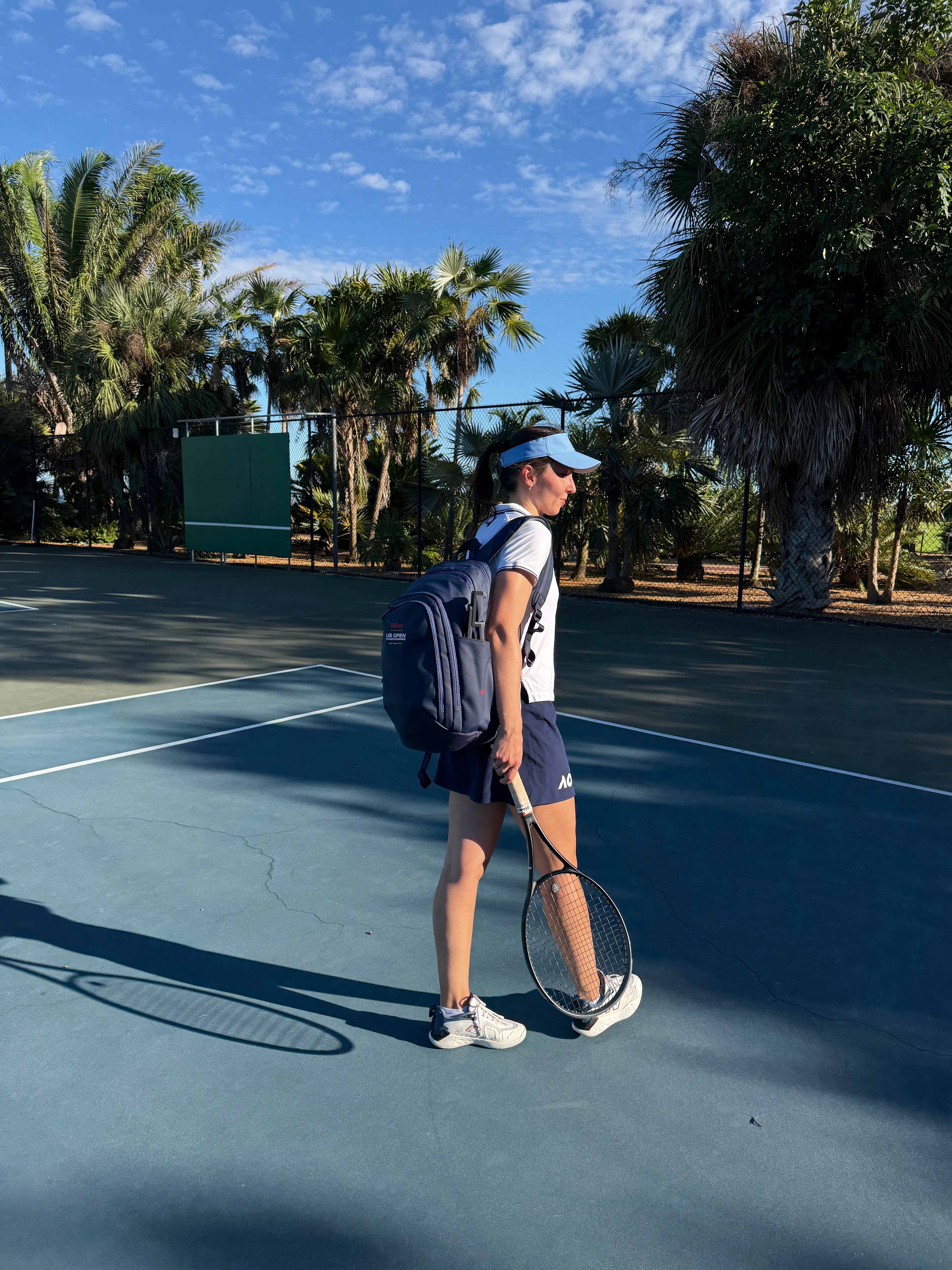 Person walking on a blue outdoor court with trees and a blue sky in the background.