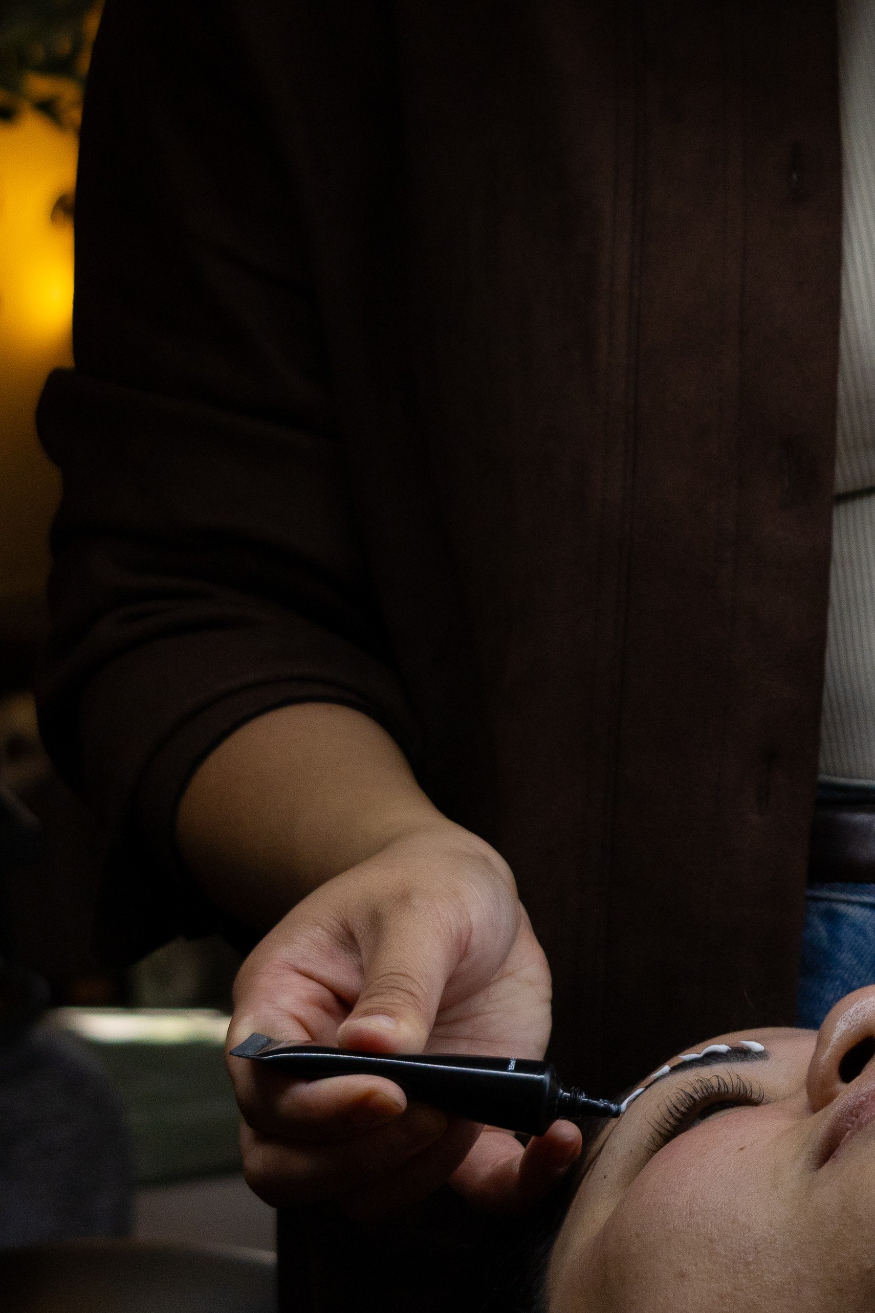 Person holding a tool near another person's face in a dimly lit environment.