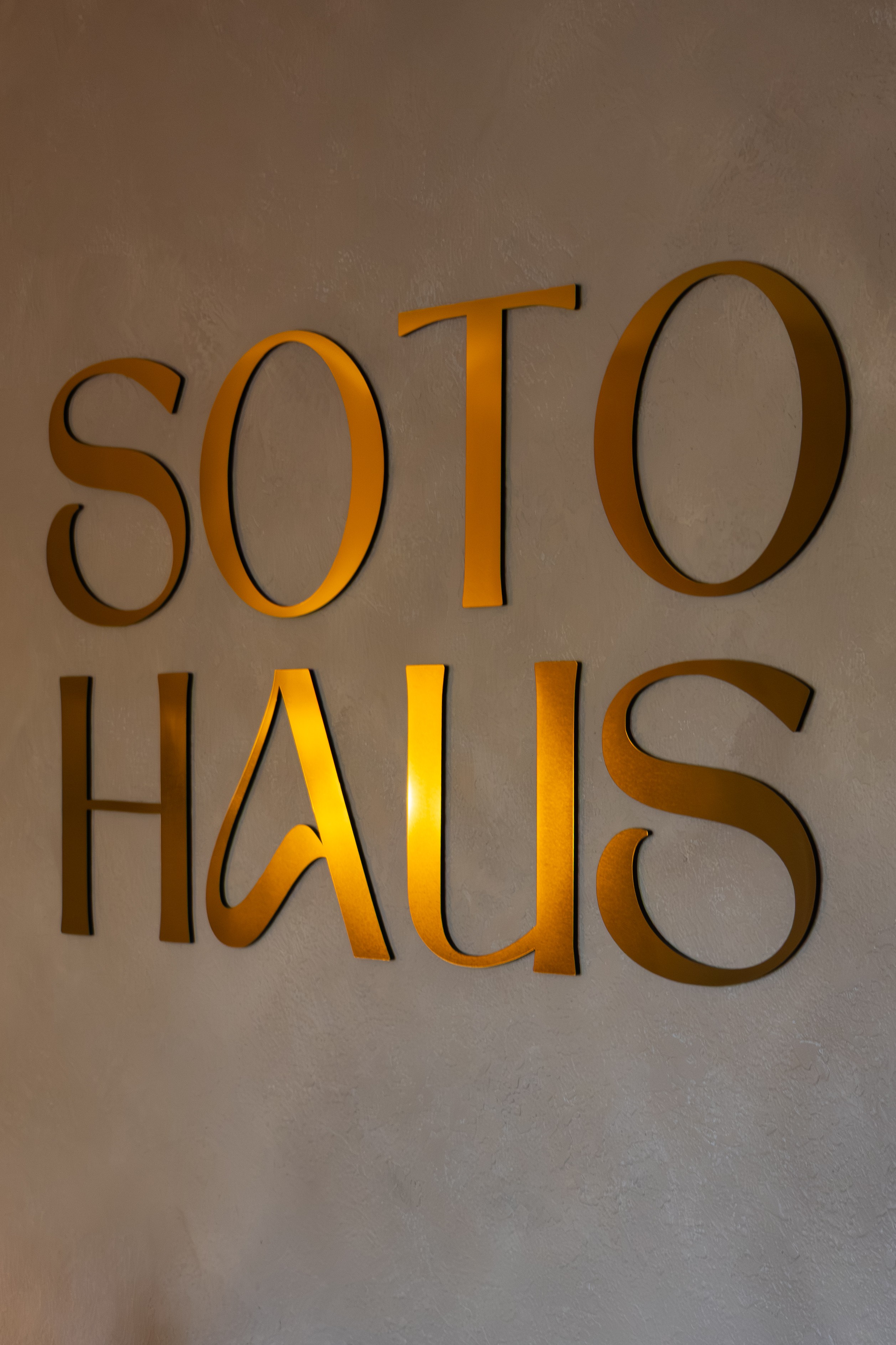 Gold-colored 3D letters spell 'SOTO HAUS' on a plain wall.