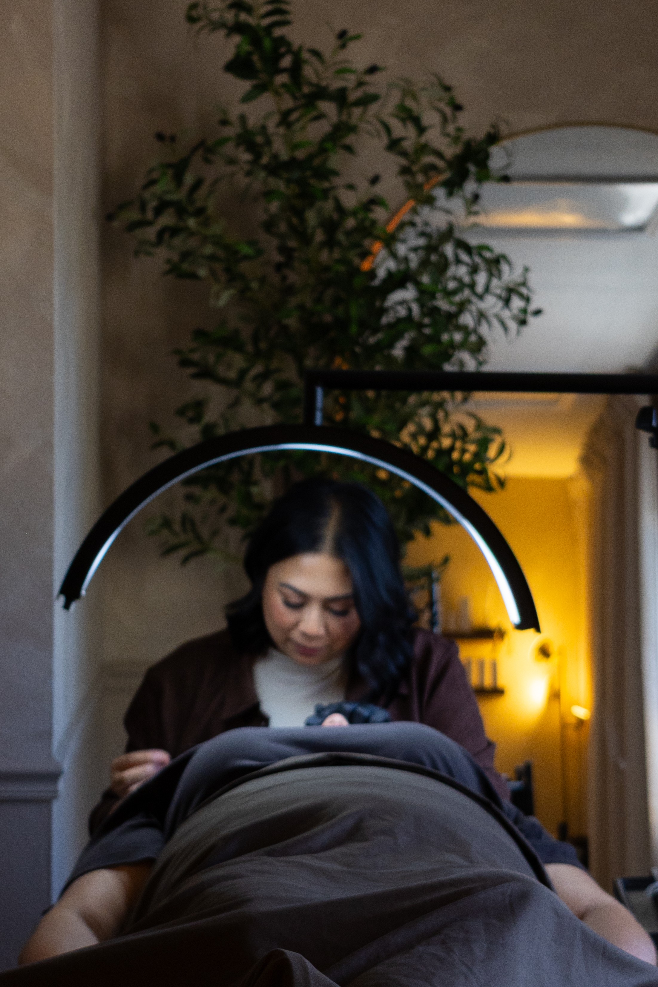 Woman sitting at a table, looking at her phone, with a large circular light above her head, in a cozy indoor setting.