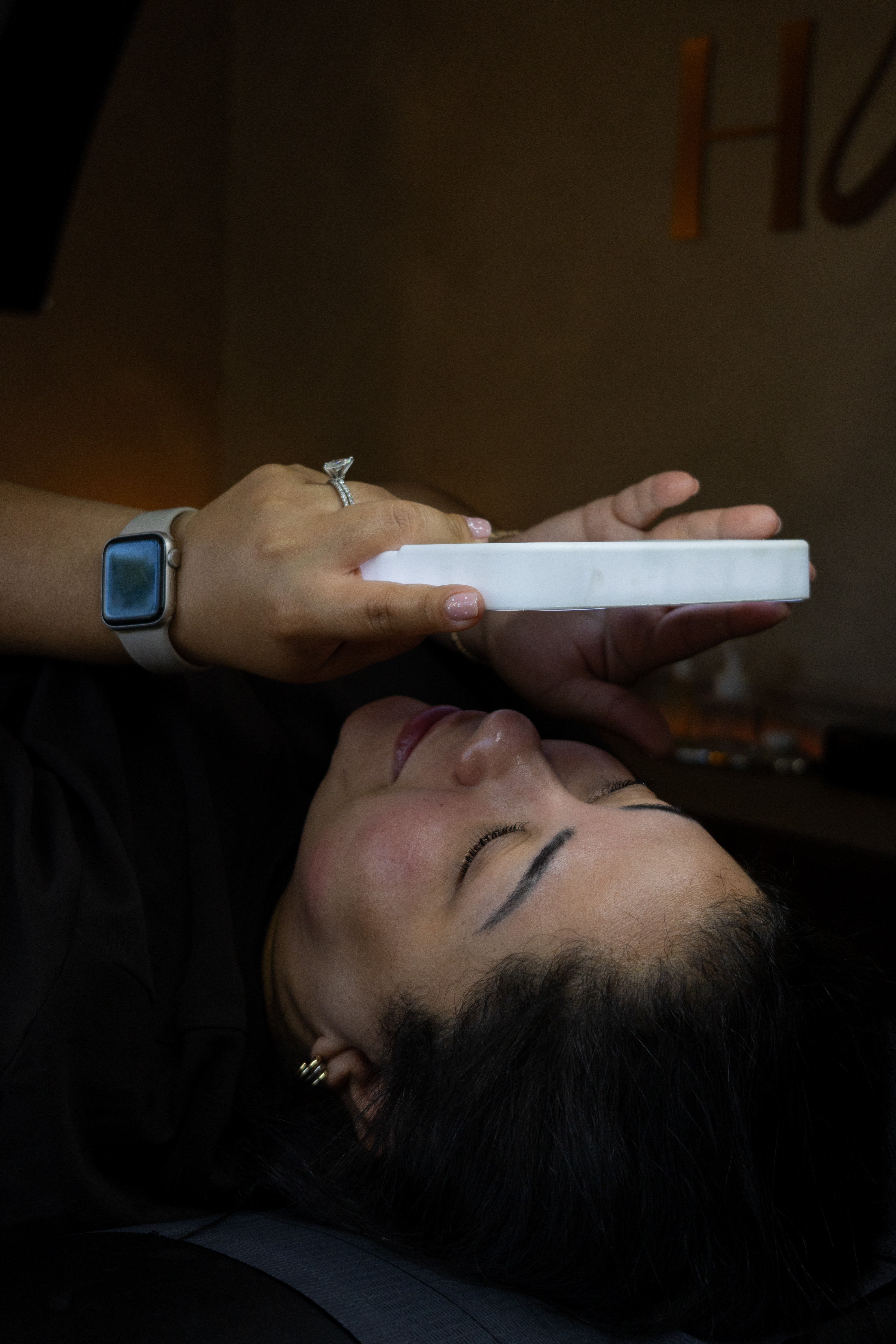 Person lying down holding a rectangular object, with face turned upward and eyes closed.