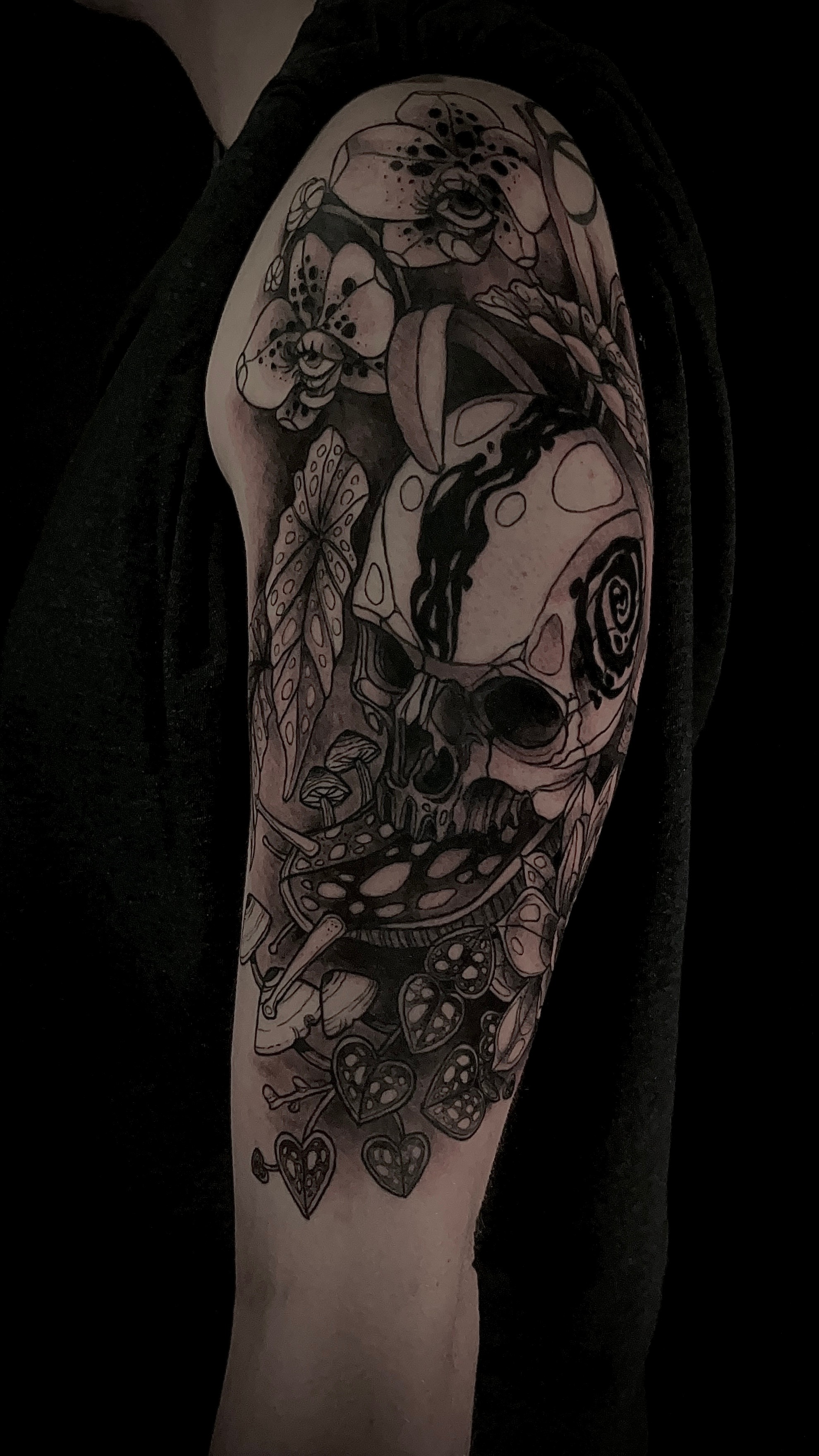 Tattoo sleeve featuring skulls, flowers, and abstract designs on person's upper arm.