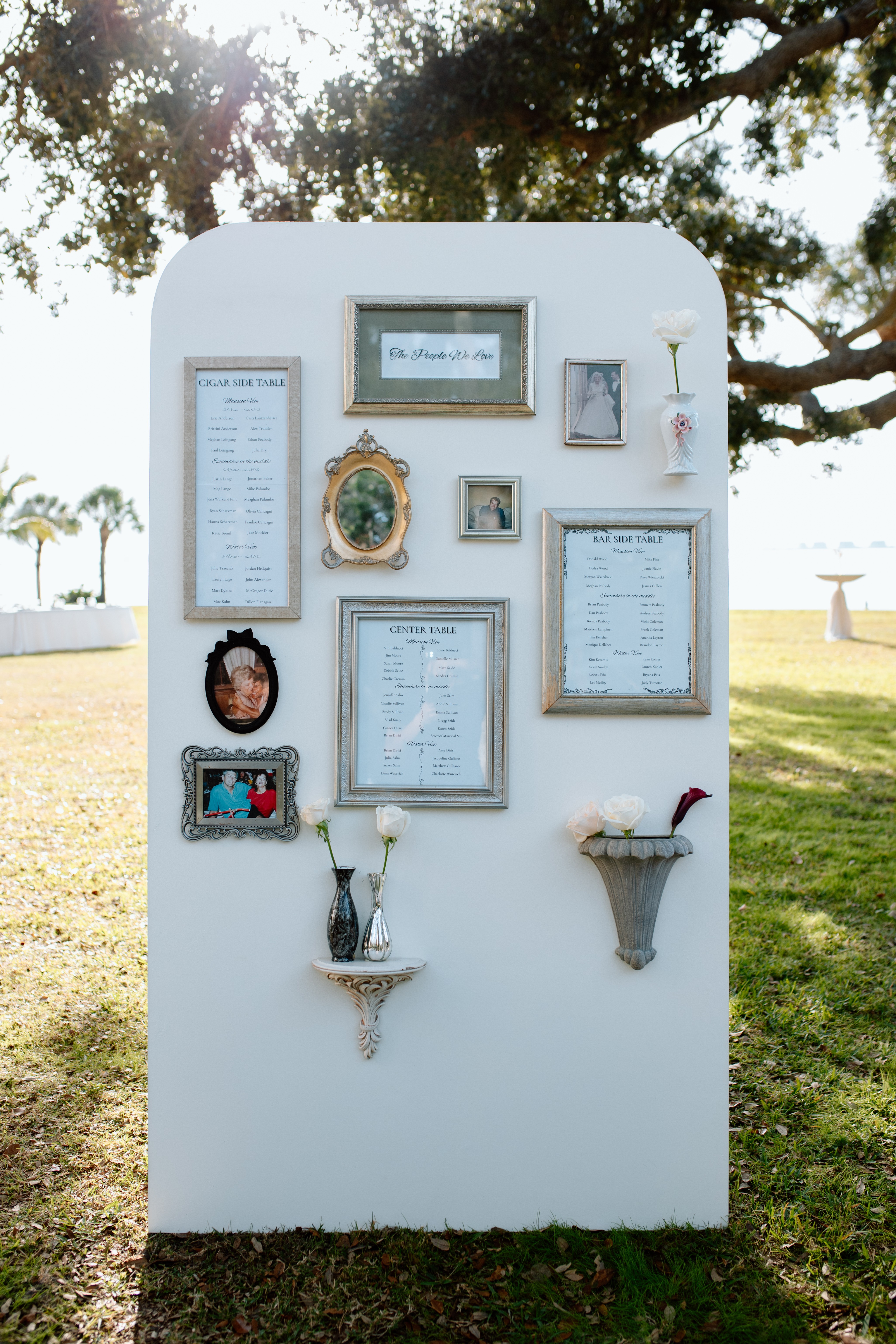 Display board with framed pictures and documents outdoors, trees and grass in background, sunlight filtering through leaves.