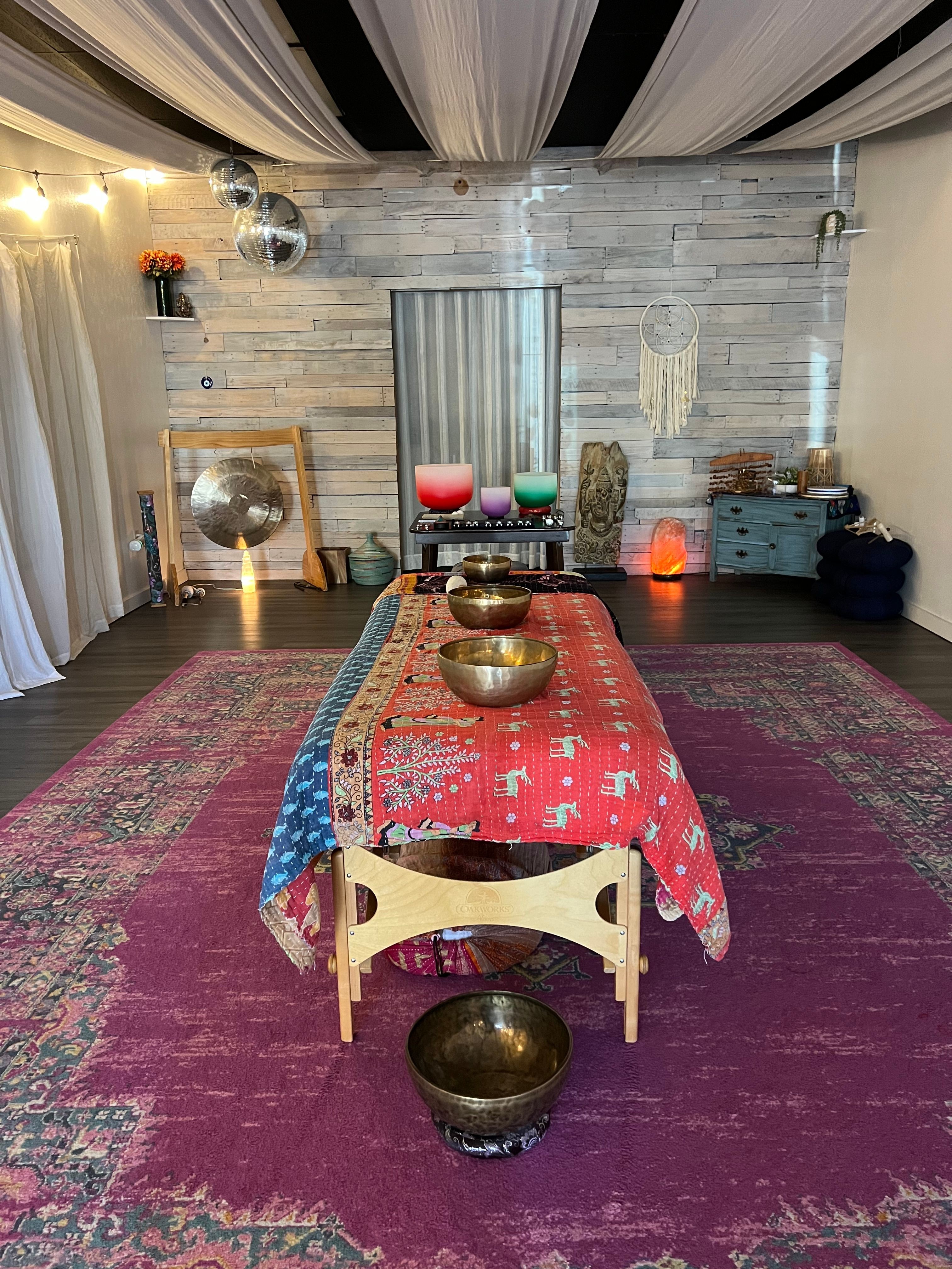 A room with a colorful rug, a low table with a patterned cloth, and various objects including bowls and candles.