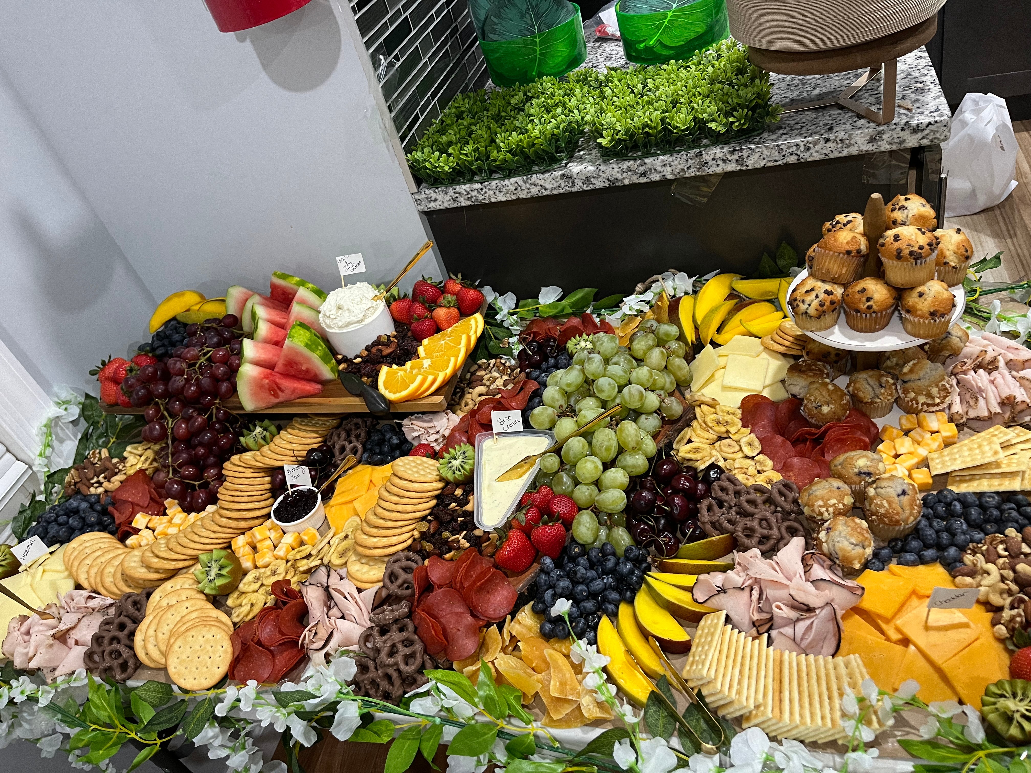 Assorted fruits, cookies, and cheese on a table with greenery in the background.