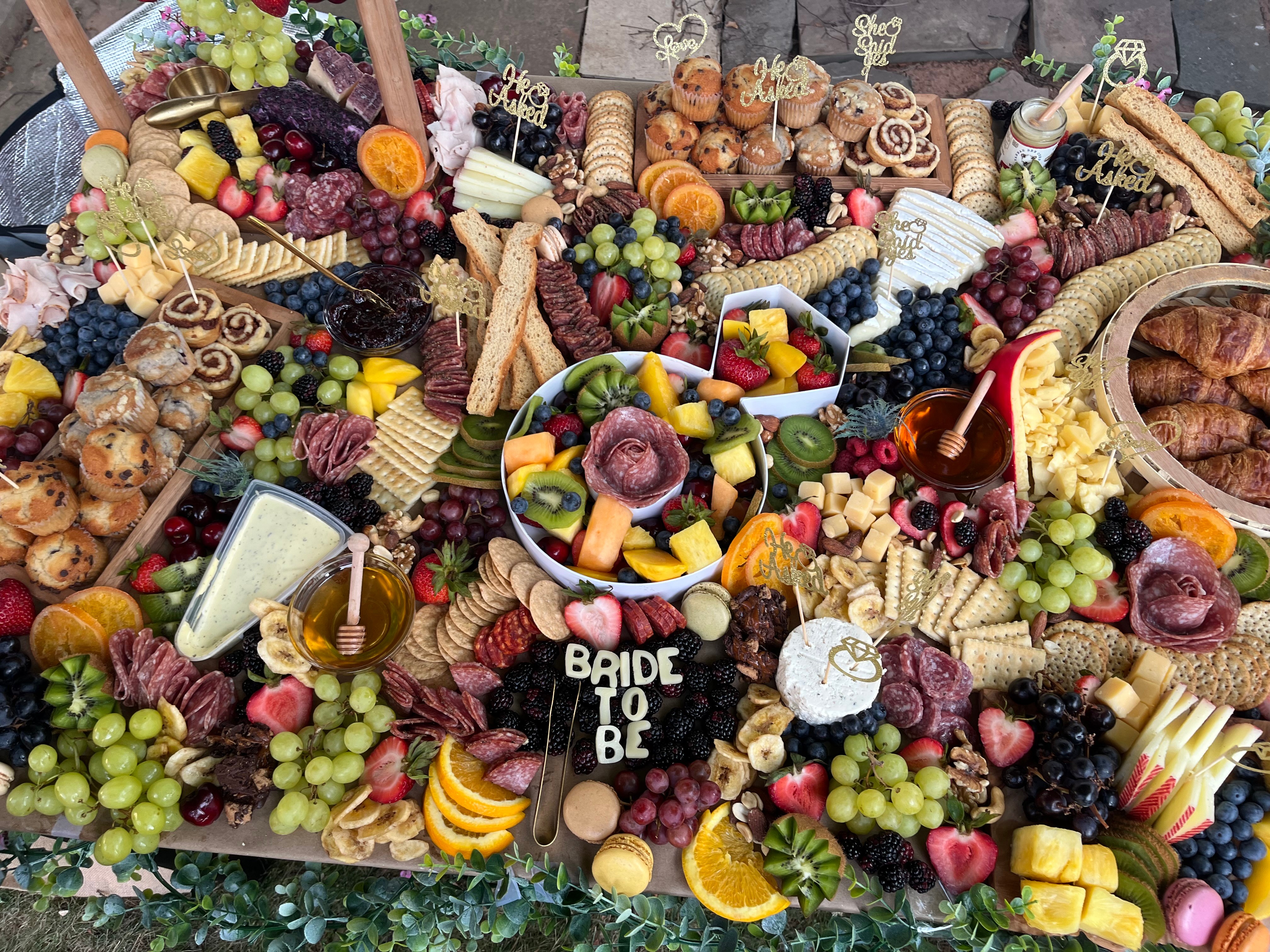 Assorted fruits, cheeses, and snacks arranged on a table with a sign reading 'Bride to Be'.