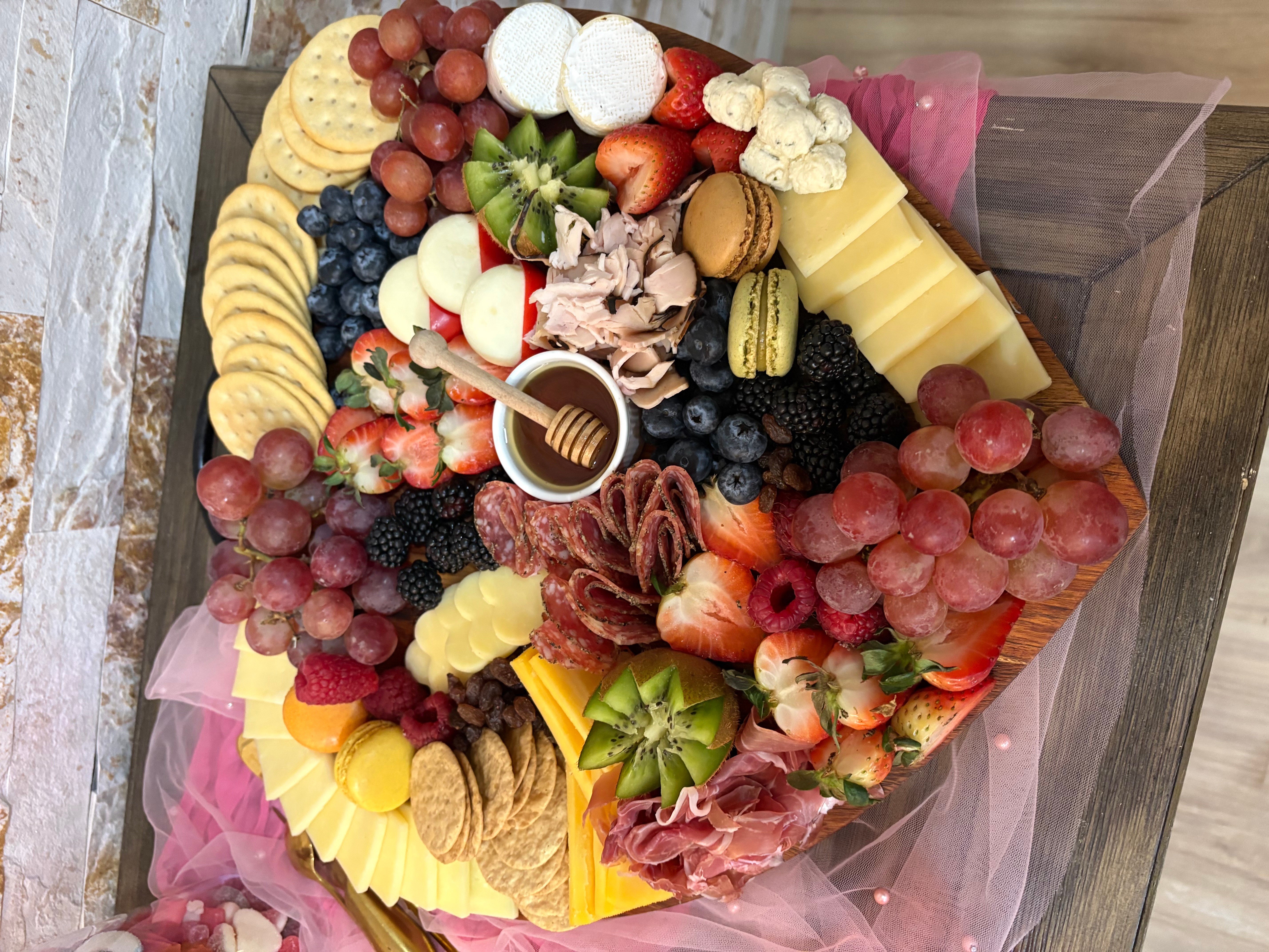 Colorful fruit and cheese bouquet with grapes, strawberries, blueberries, cheese slices, and crackers, arranged on pink tissue paper.