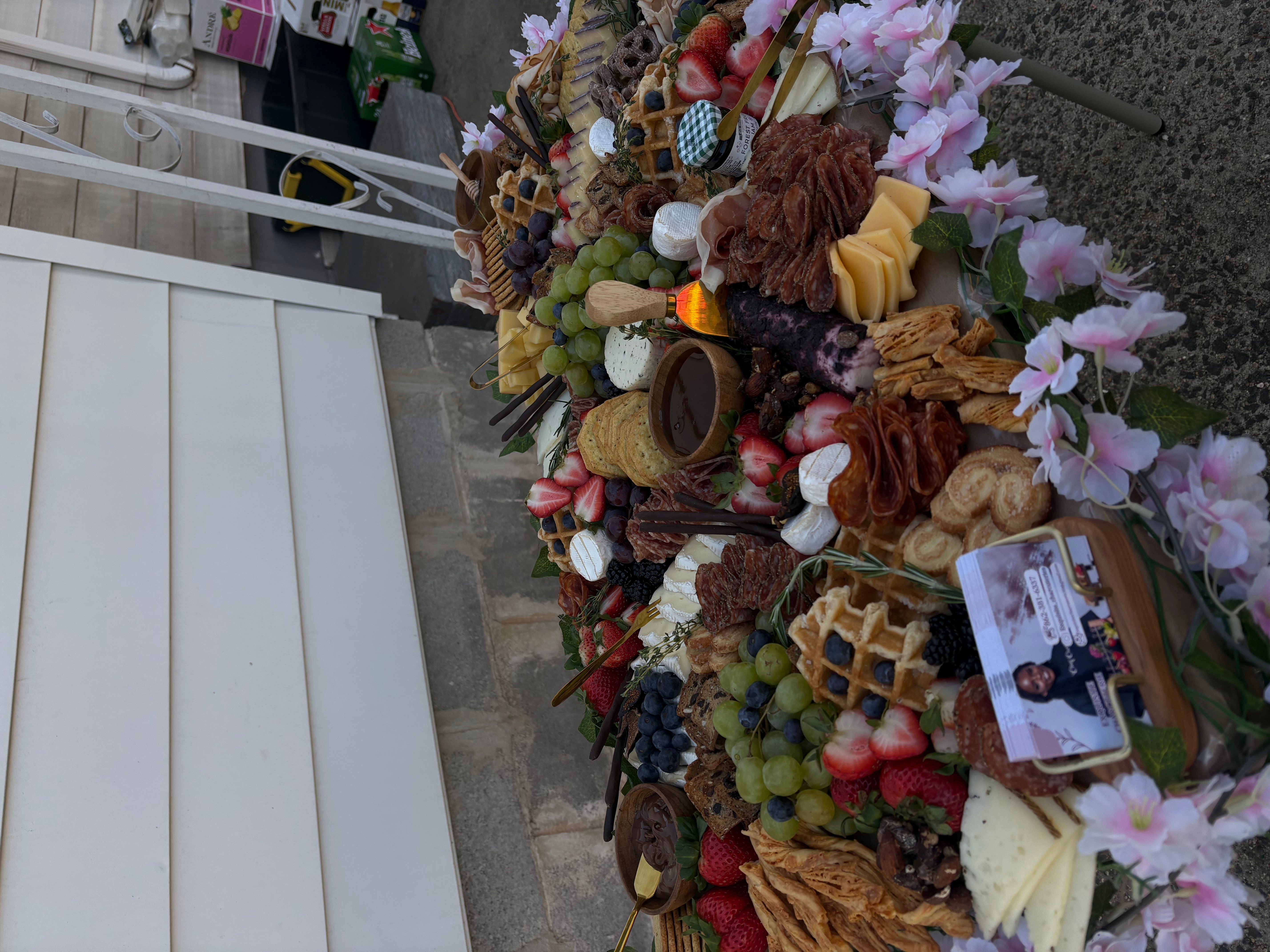 Flowers, fruits, and a photo on a memorial or tribute display, with a white structure in the background.