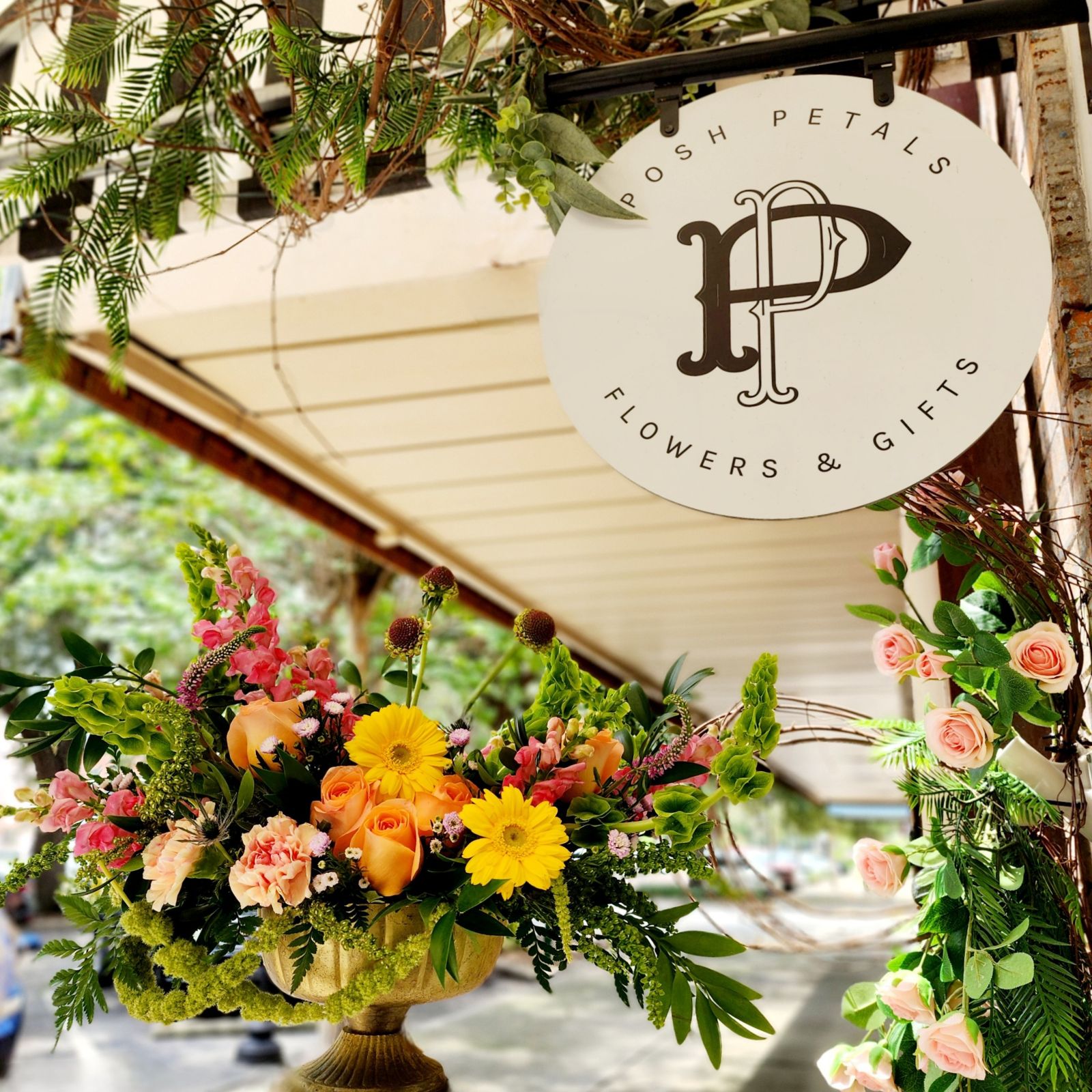 Flower shop sign with floral arrangements and greenery outside a store, reading 'Posh Petals Flowers & Gifts'.
