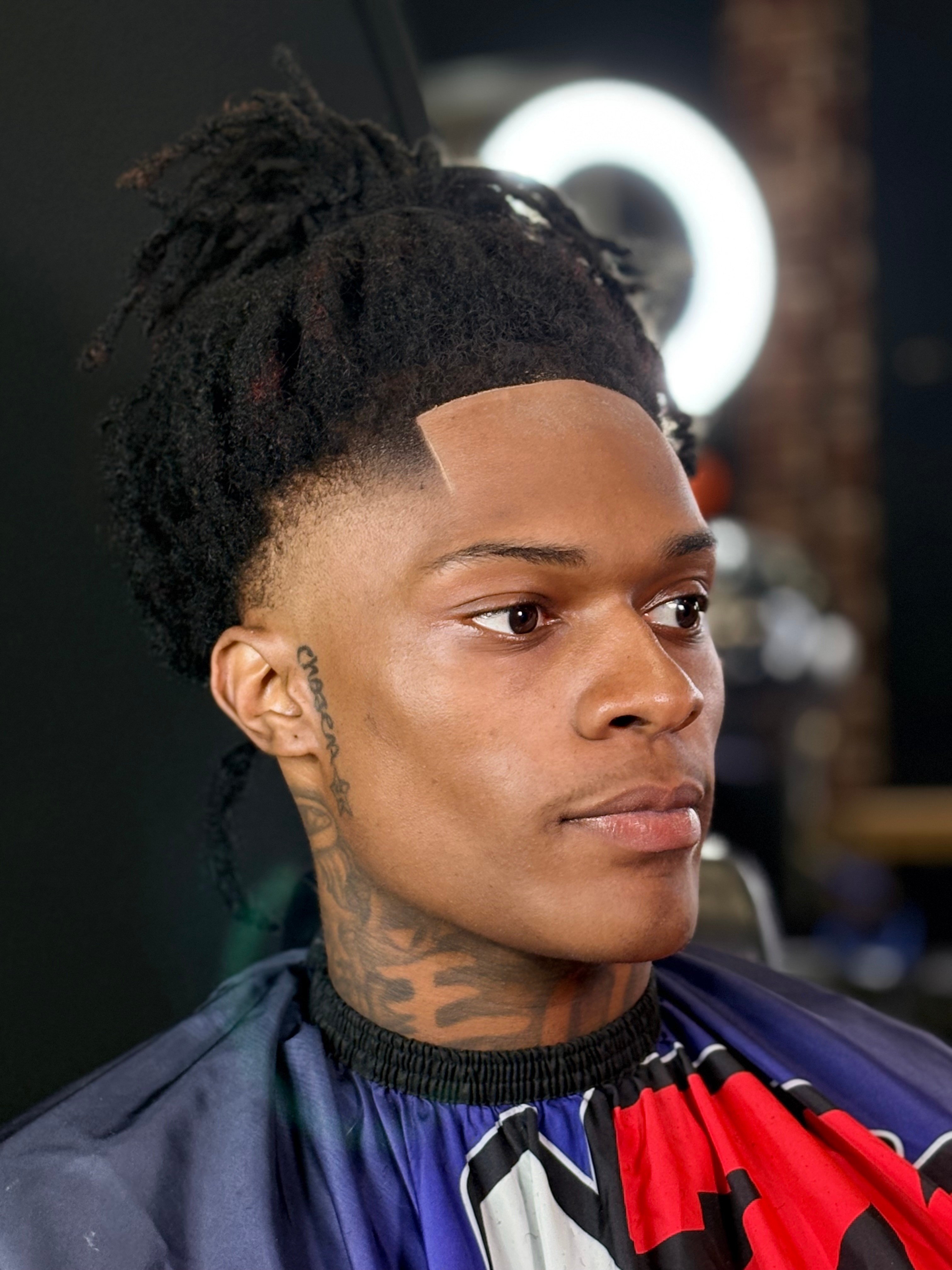 Woman with styled dreadlocks and tattoos on neck, wearing a cape, in a salon setting.