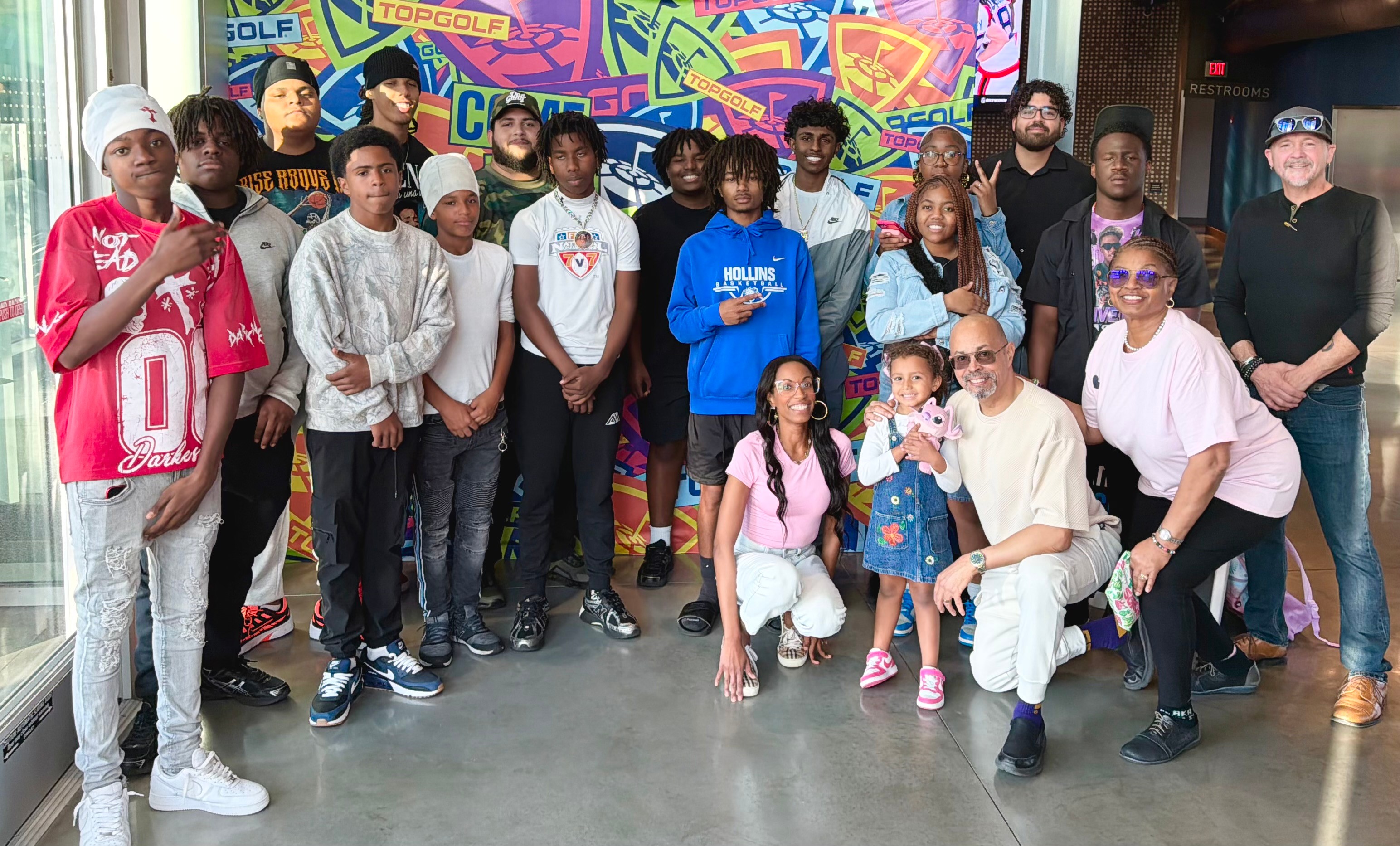 Group of children and adults standing together indoors in front of colorful graffiti-style background.