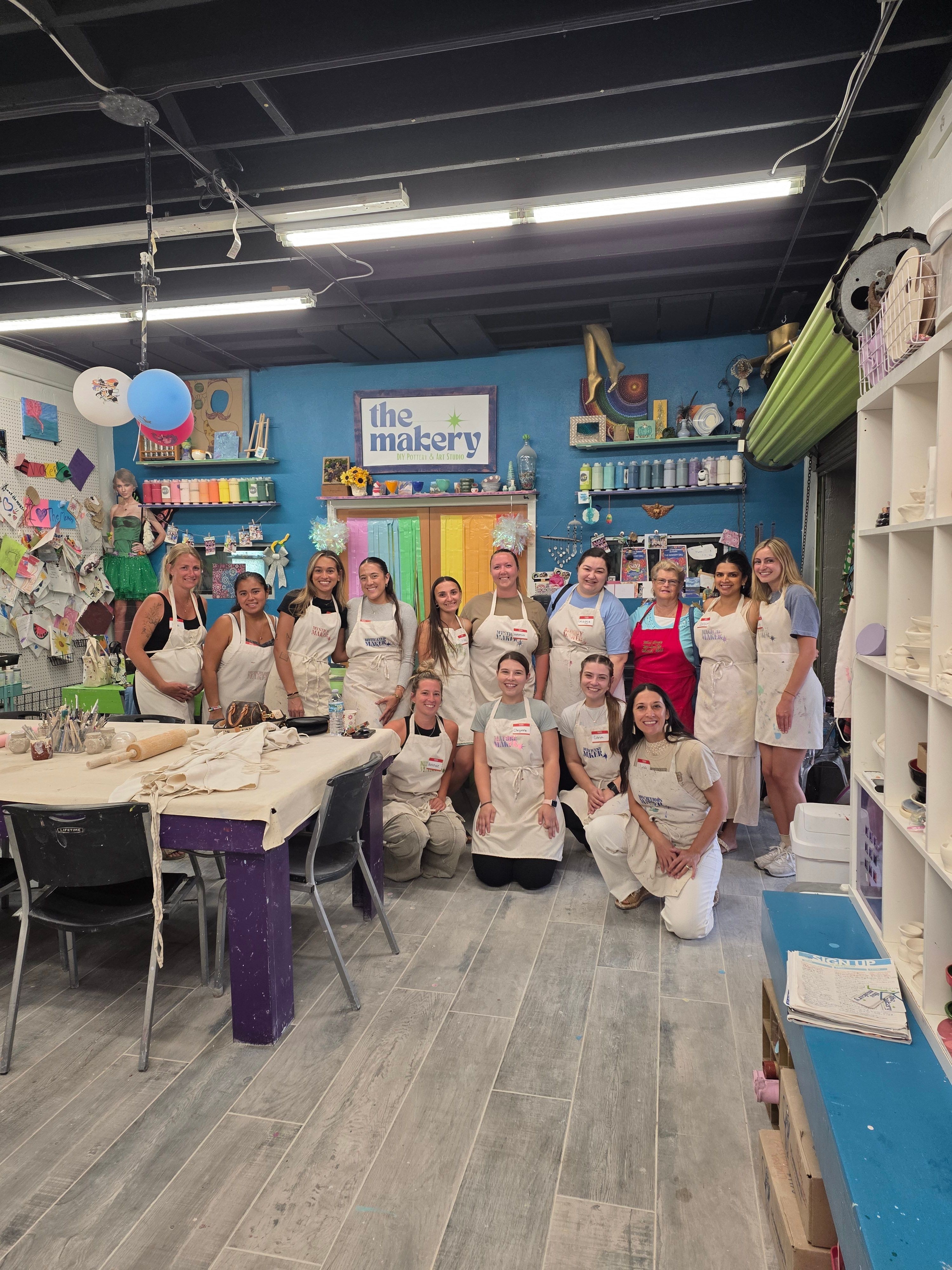 Group of children and adults gathered around a table in a colorful room with shelves and decorations.