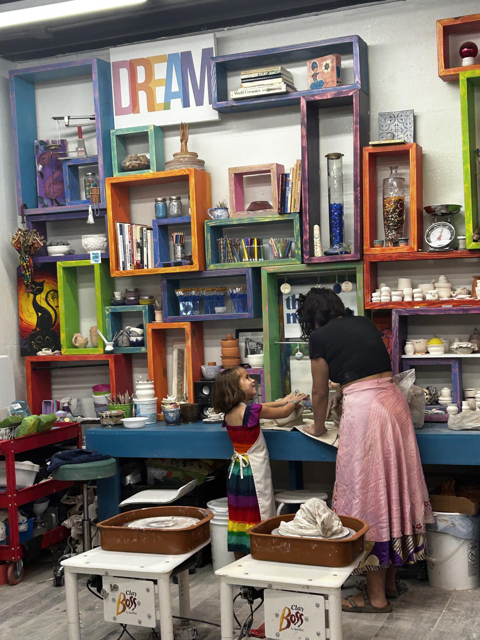 Child and adult at a colorful display shelf with books and decorative items, child reaching out to adult, shelves in various colors.